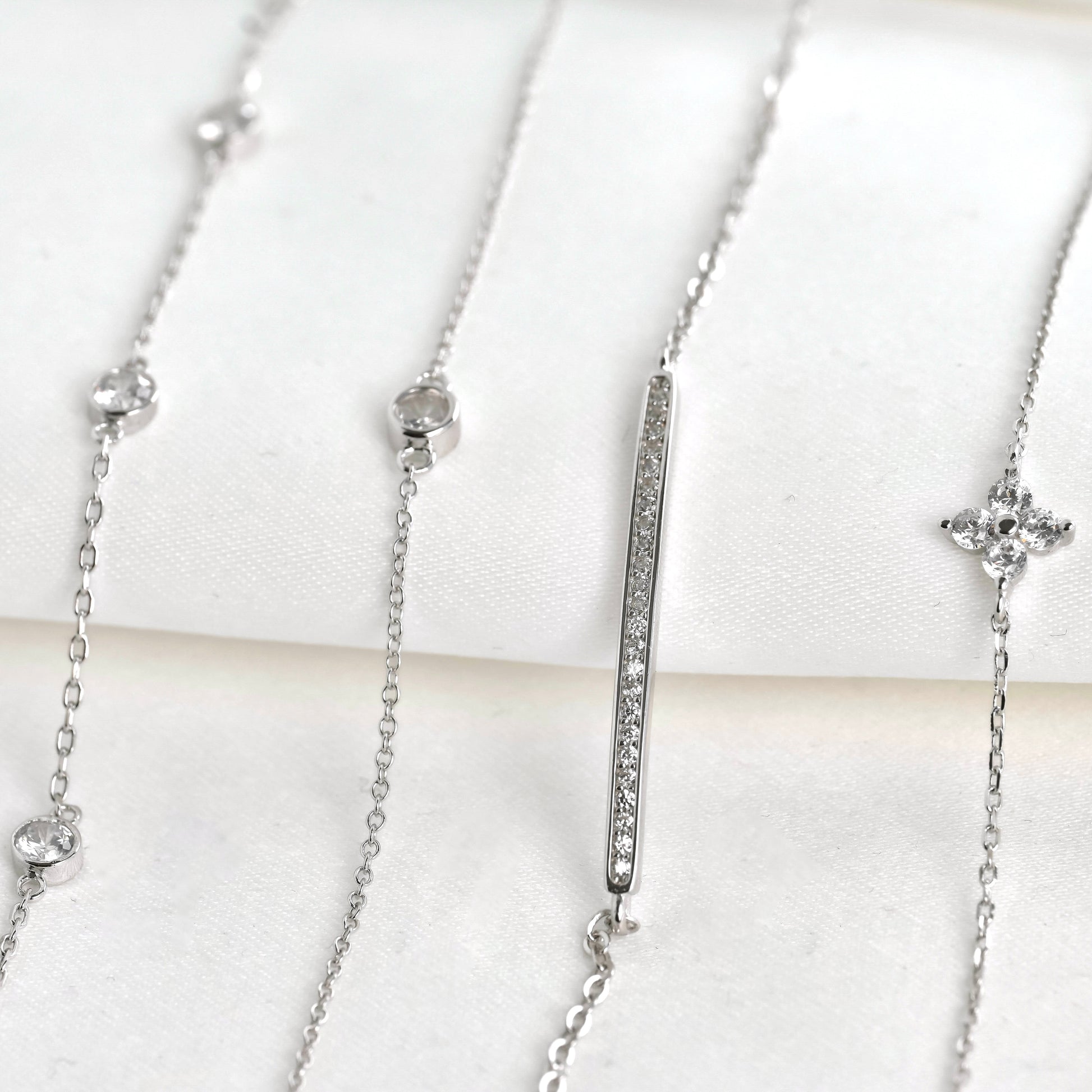 Silver bracelets with clover, bar and bezel pendants on a white background