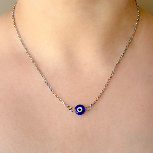 Necklace with a blue evil eye pendant on a person wearing a white top.