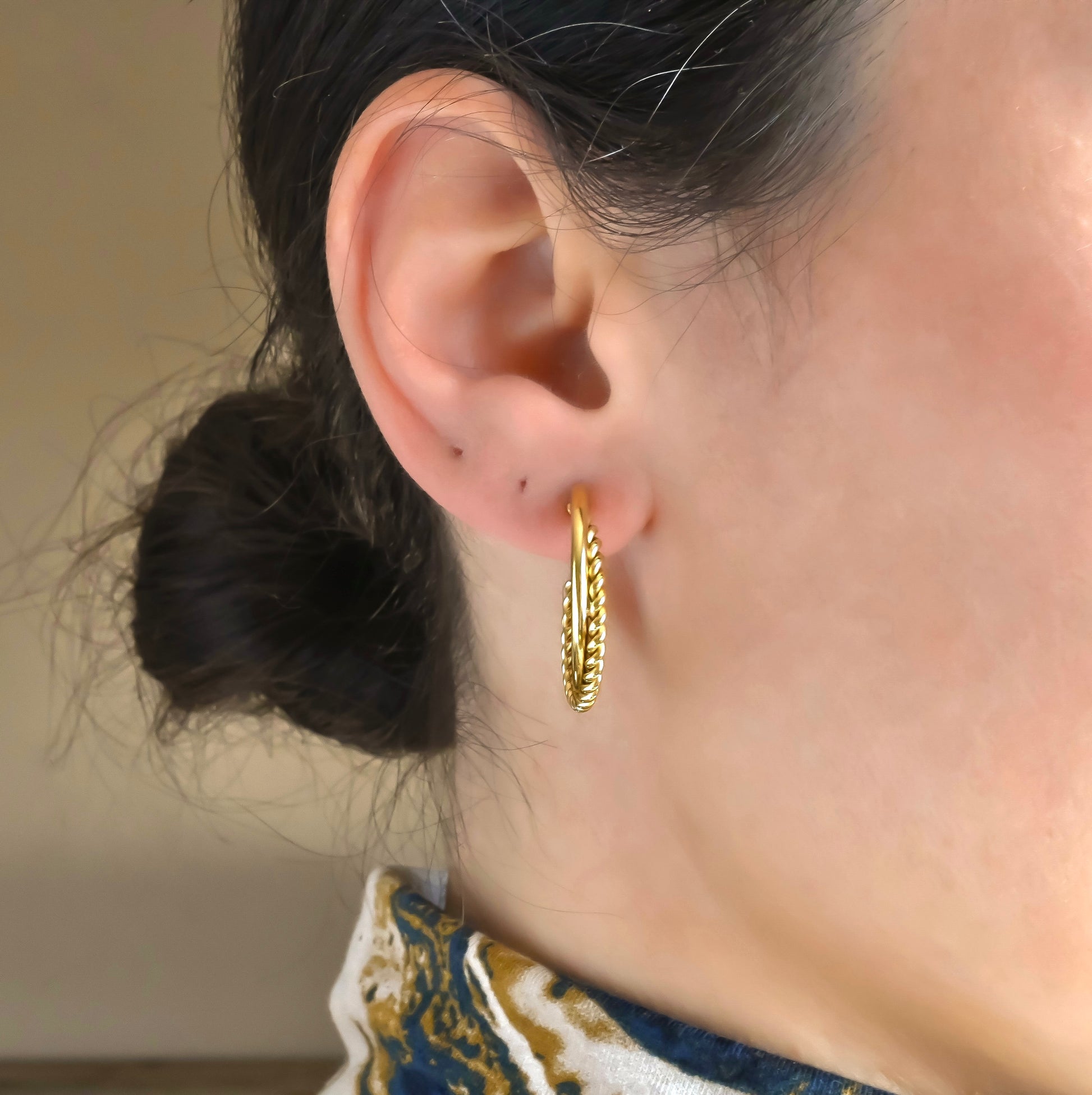 Front close-up of an ear wearing a gold hoop earring with a blurred background