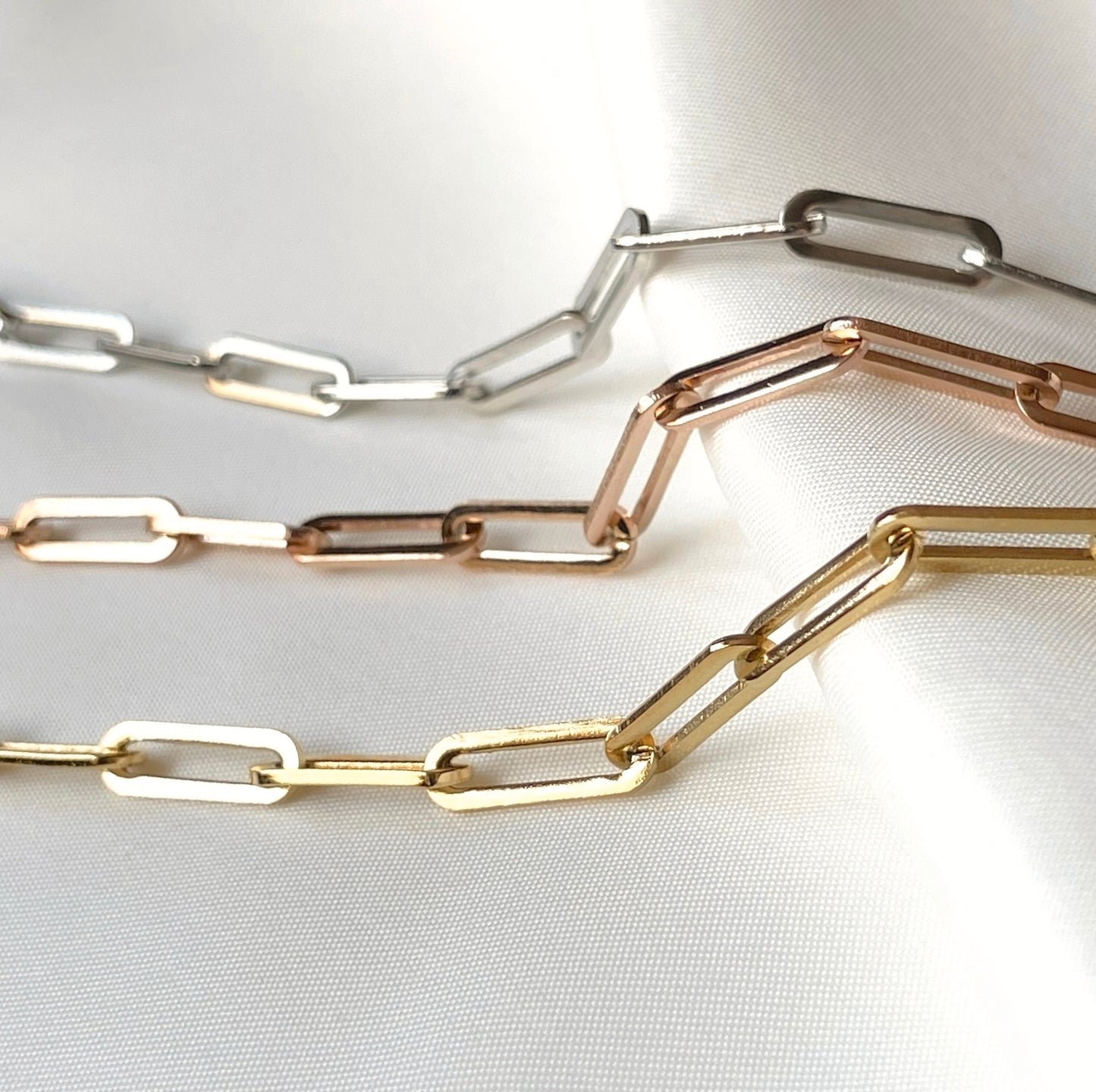 Three chunky rectangular chain necklaces in gold, rose gold, and silver on a white background