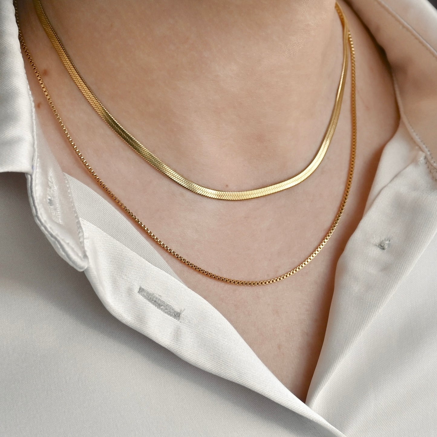 20-inch gold box chain layered with a 16" herringbone chain on a person wearing a white shirt.