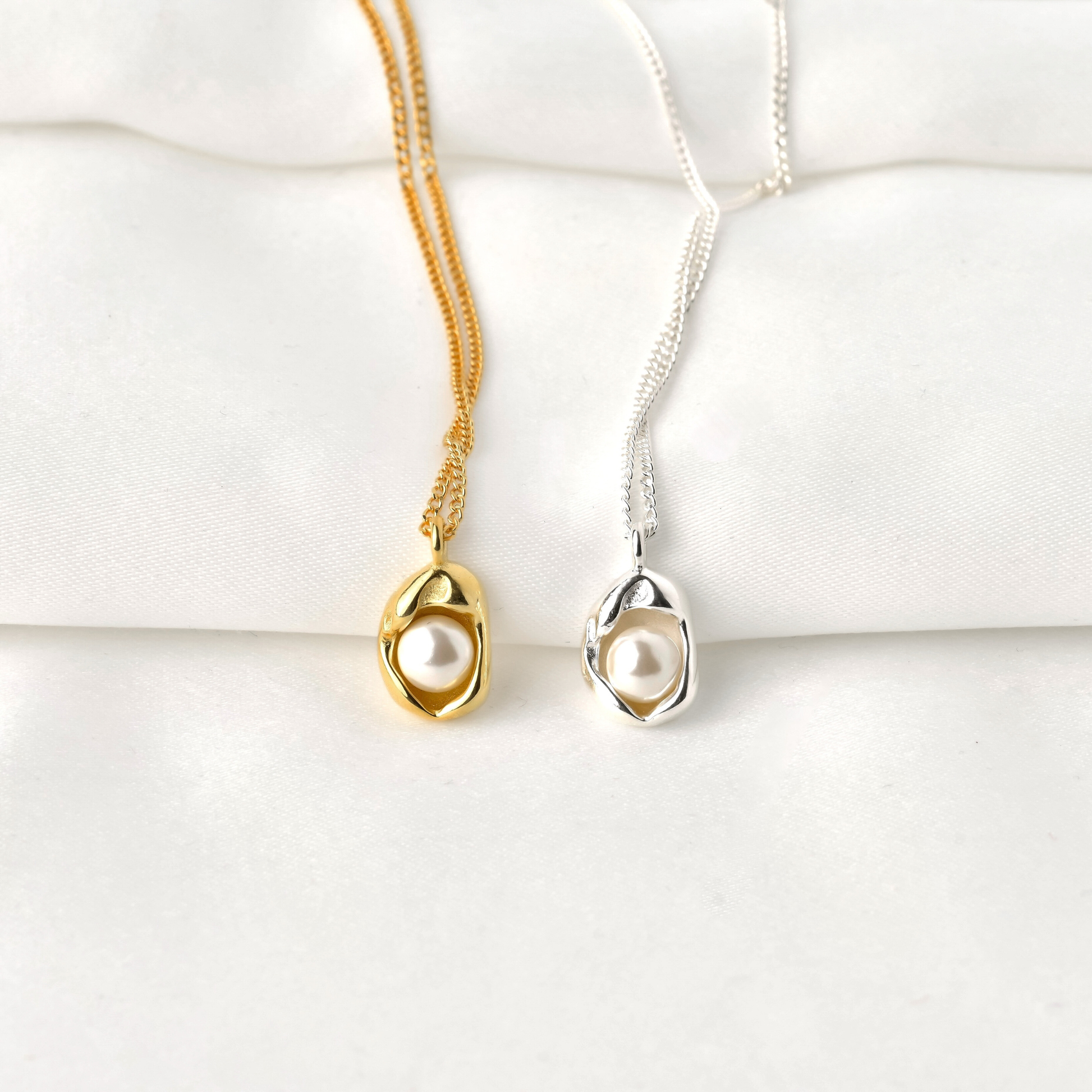 front view of Gold and silver necklaces with pearl pendants on a white surface
