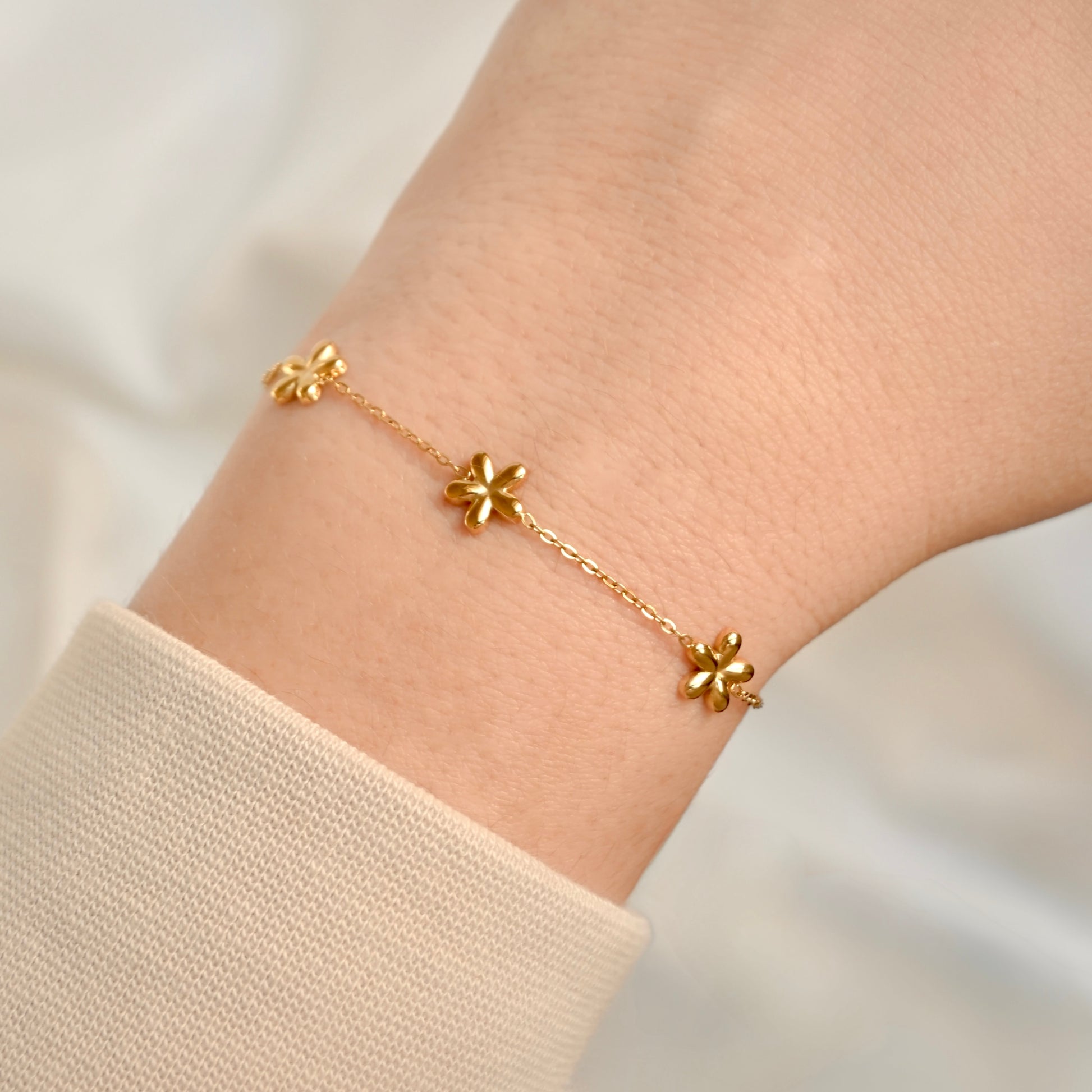 Gold flower bracelet on a wrist against a neutral background