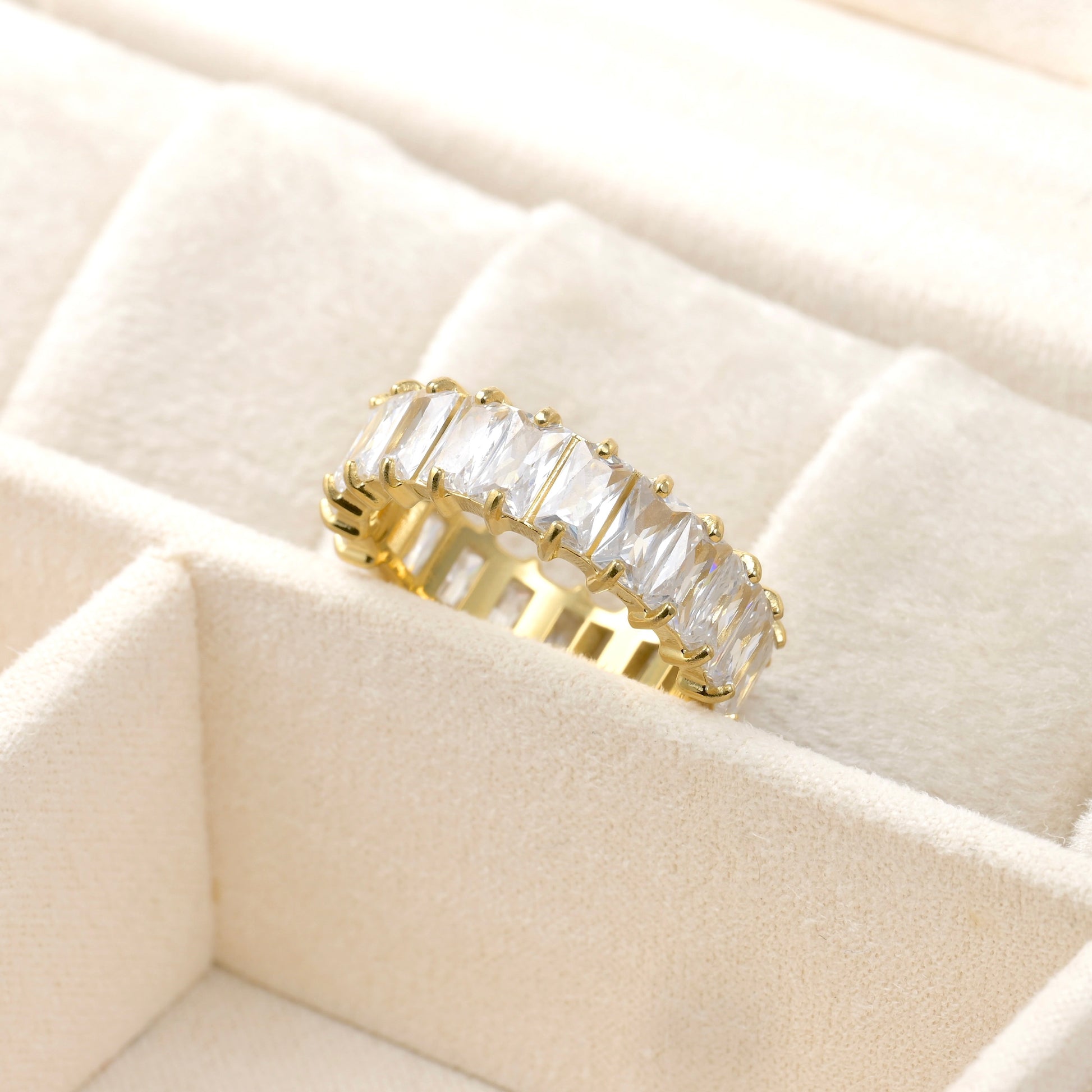 Gold eternity band with white diamonds on a beige quilted surface