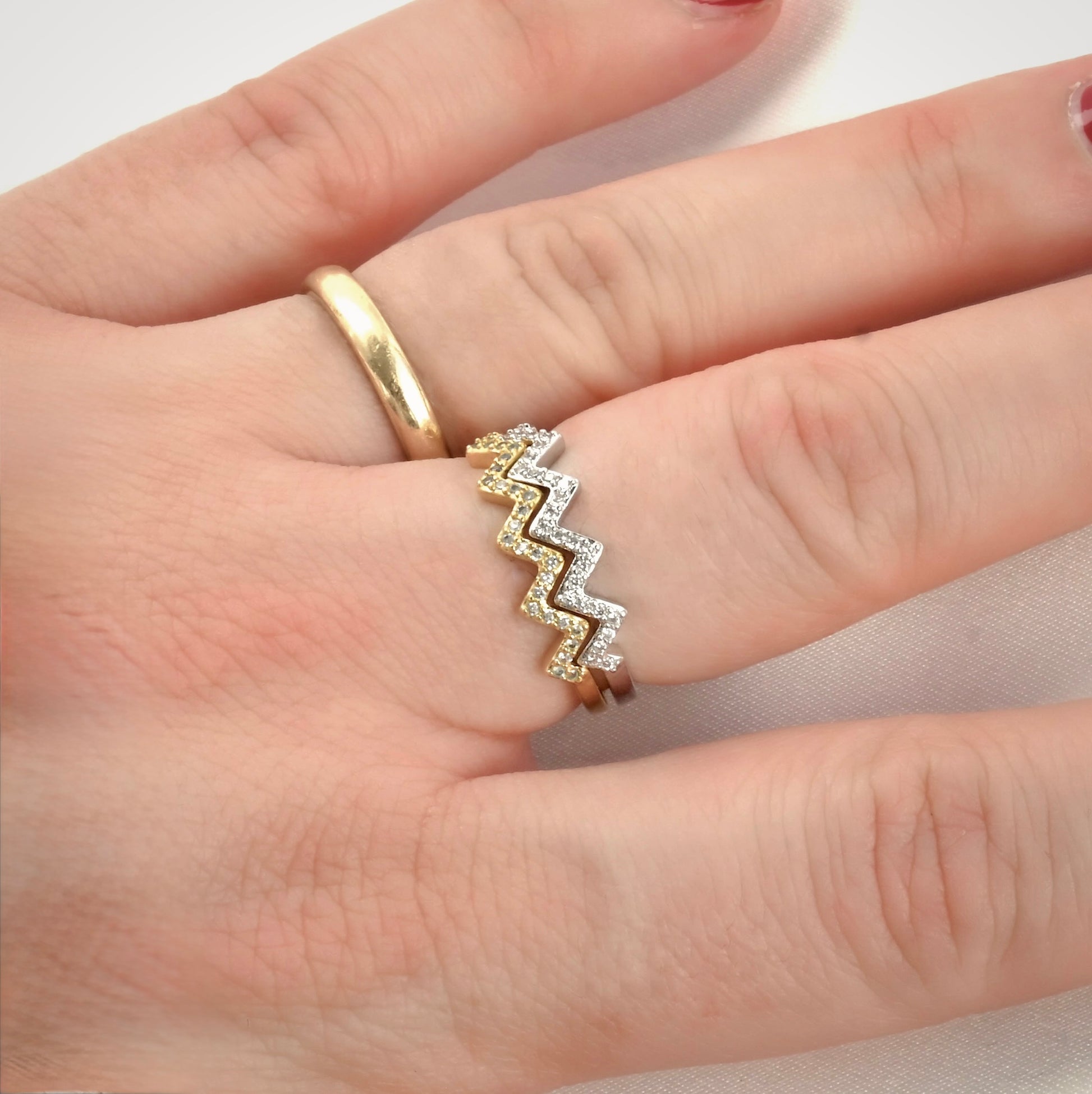 Gold and silver zigzag ring stacked on a hand against a neutral background