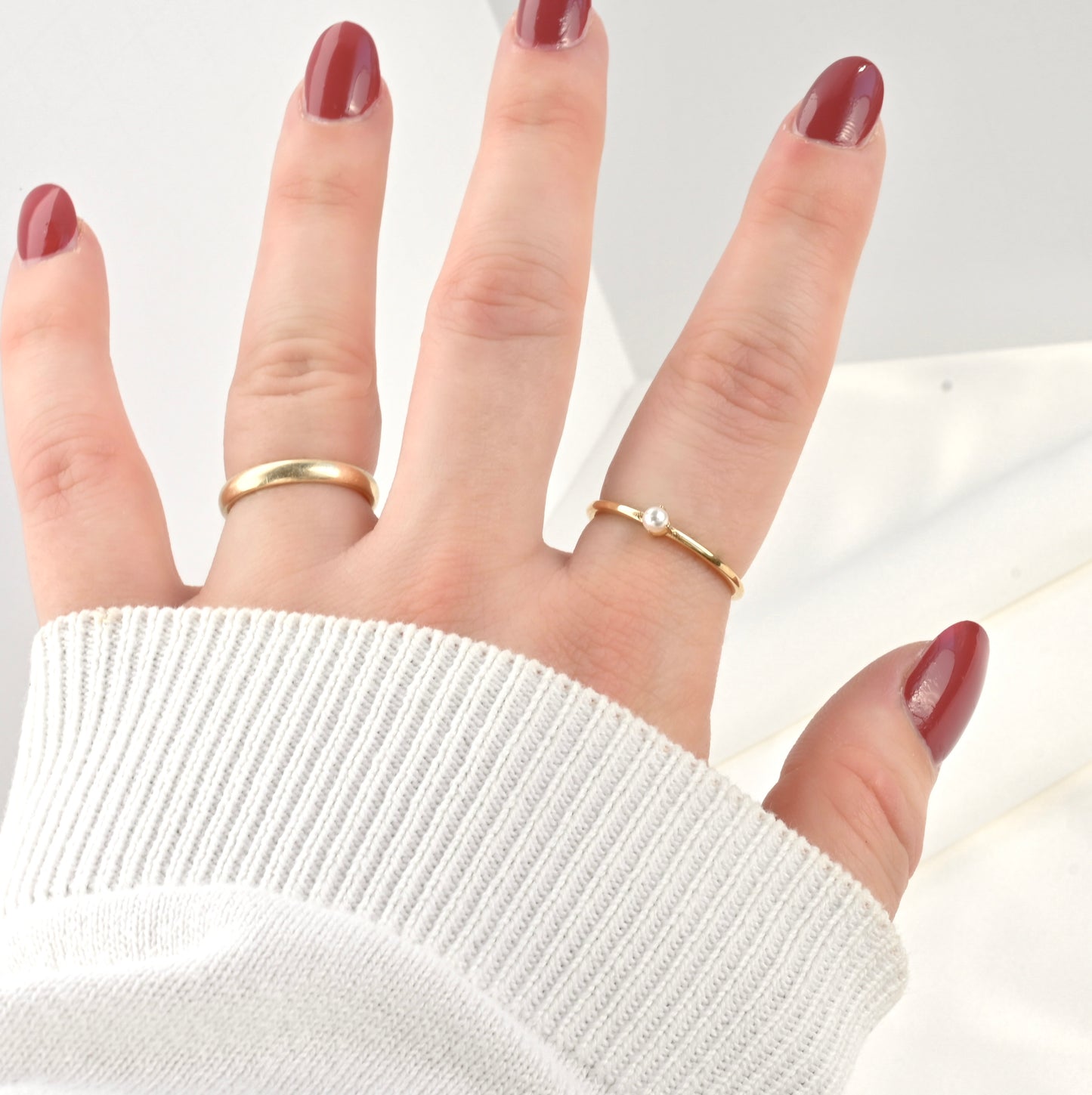 Hand wearing two gold rings with a plain background