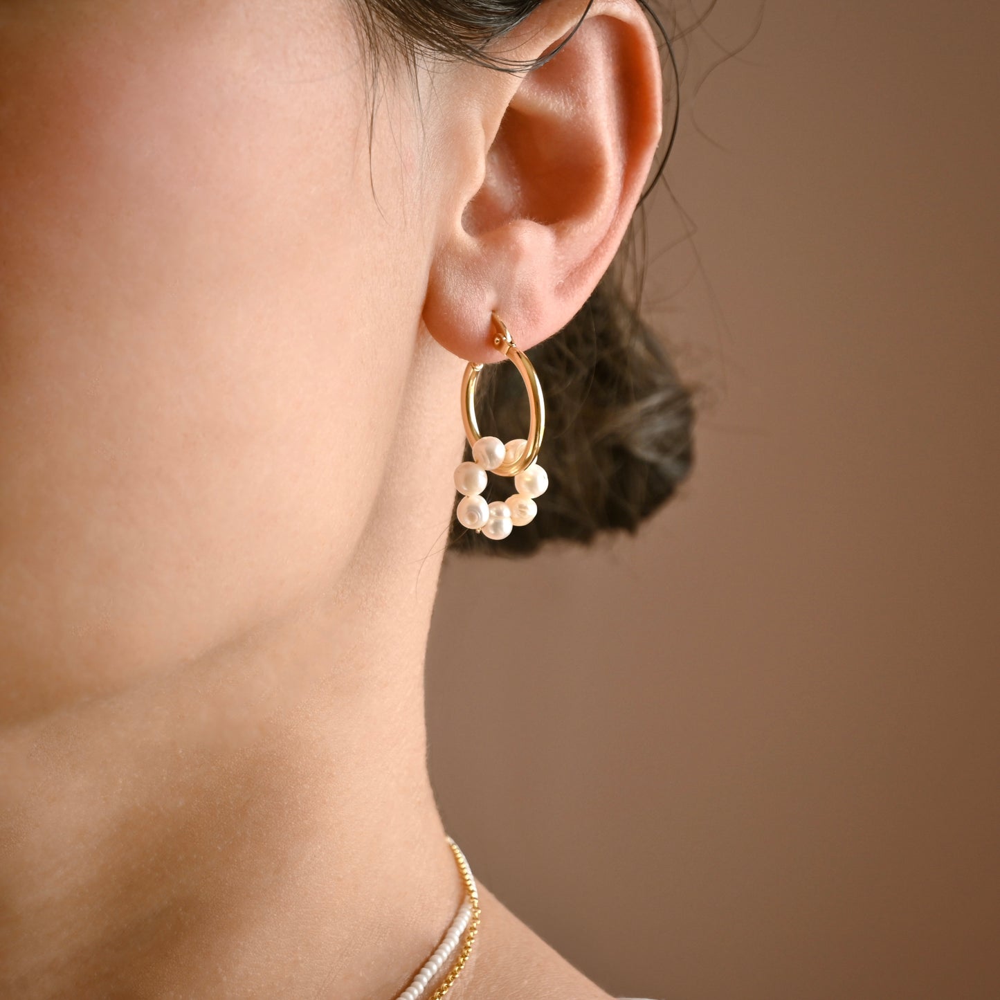 Close-up of an ear wearing a gold earring with freshwater pearl circle drop on a neutral background