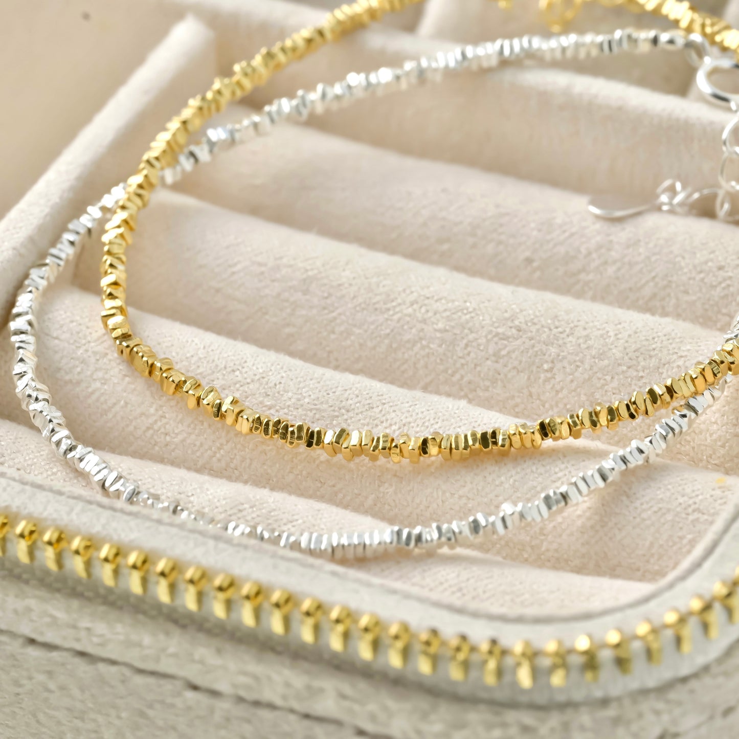 Two gold and silver beaded bracelets on a textured beige surface