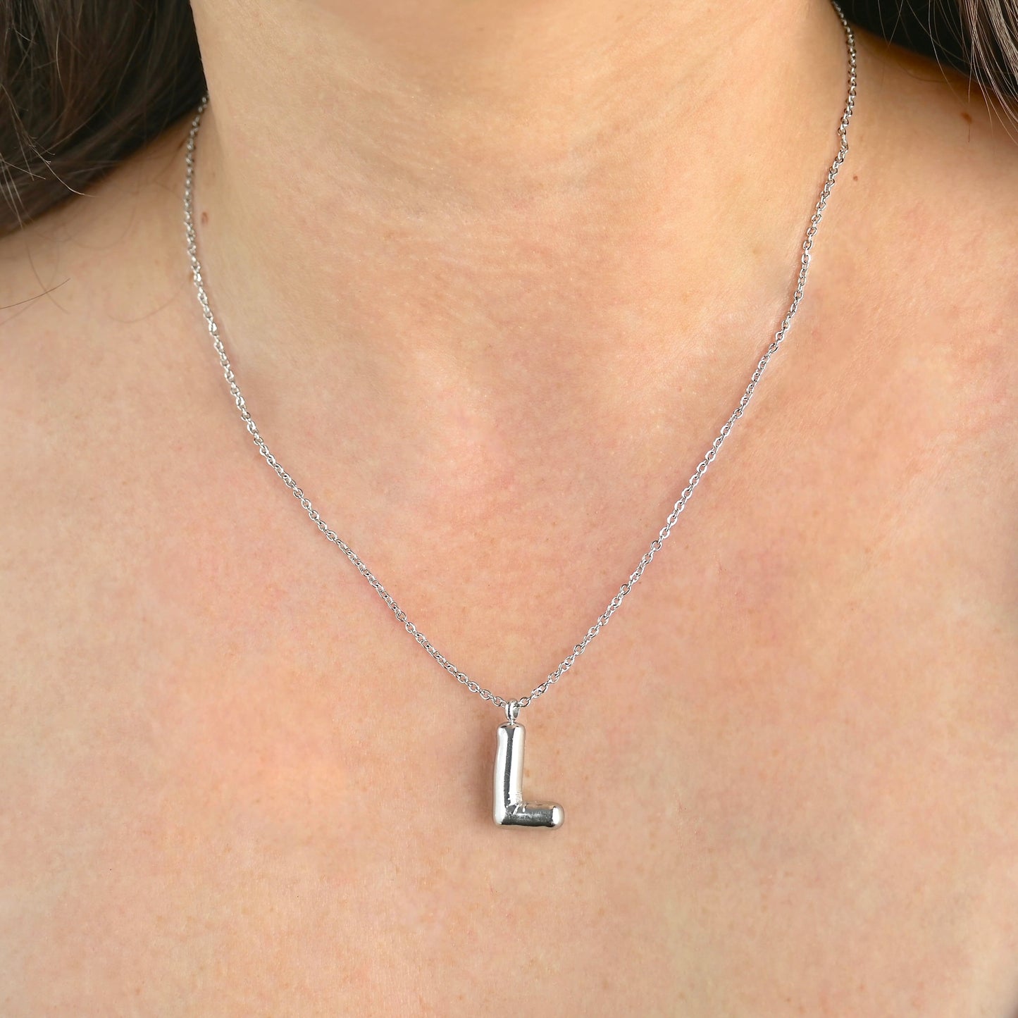 Silver initial necklace with a 'L' pendant on a person's neck