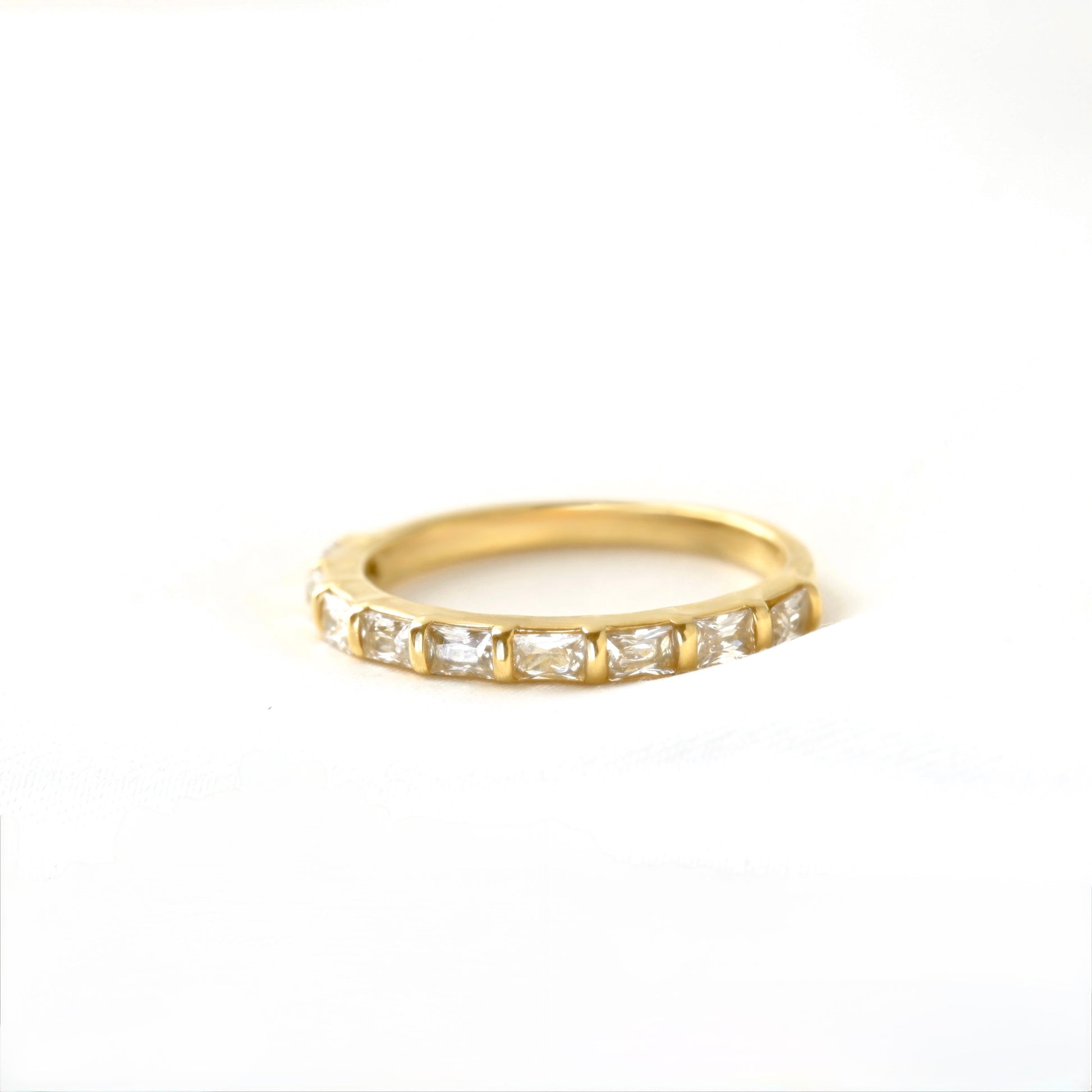 A yellow gold half eternity ring featuring a row of baguette-cut clear gemstones, photographed on a seamless white background.