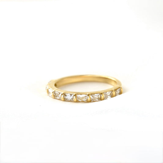A yellow gold half eternity ring featuring a row of baguette-cut clear gemstones, photographed on a seamless white background.