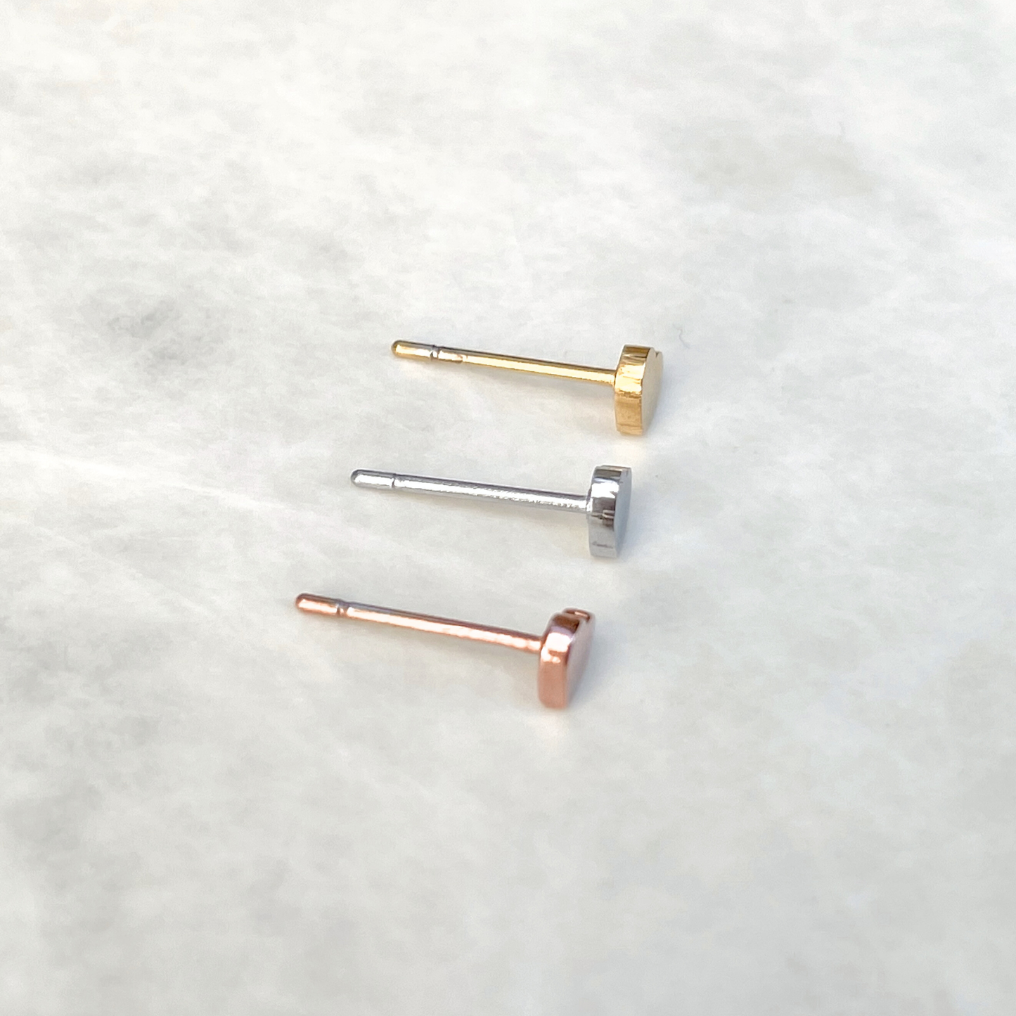 Top view of three heart earrings in gold, silver, and rose gold on a light background