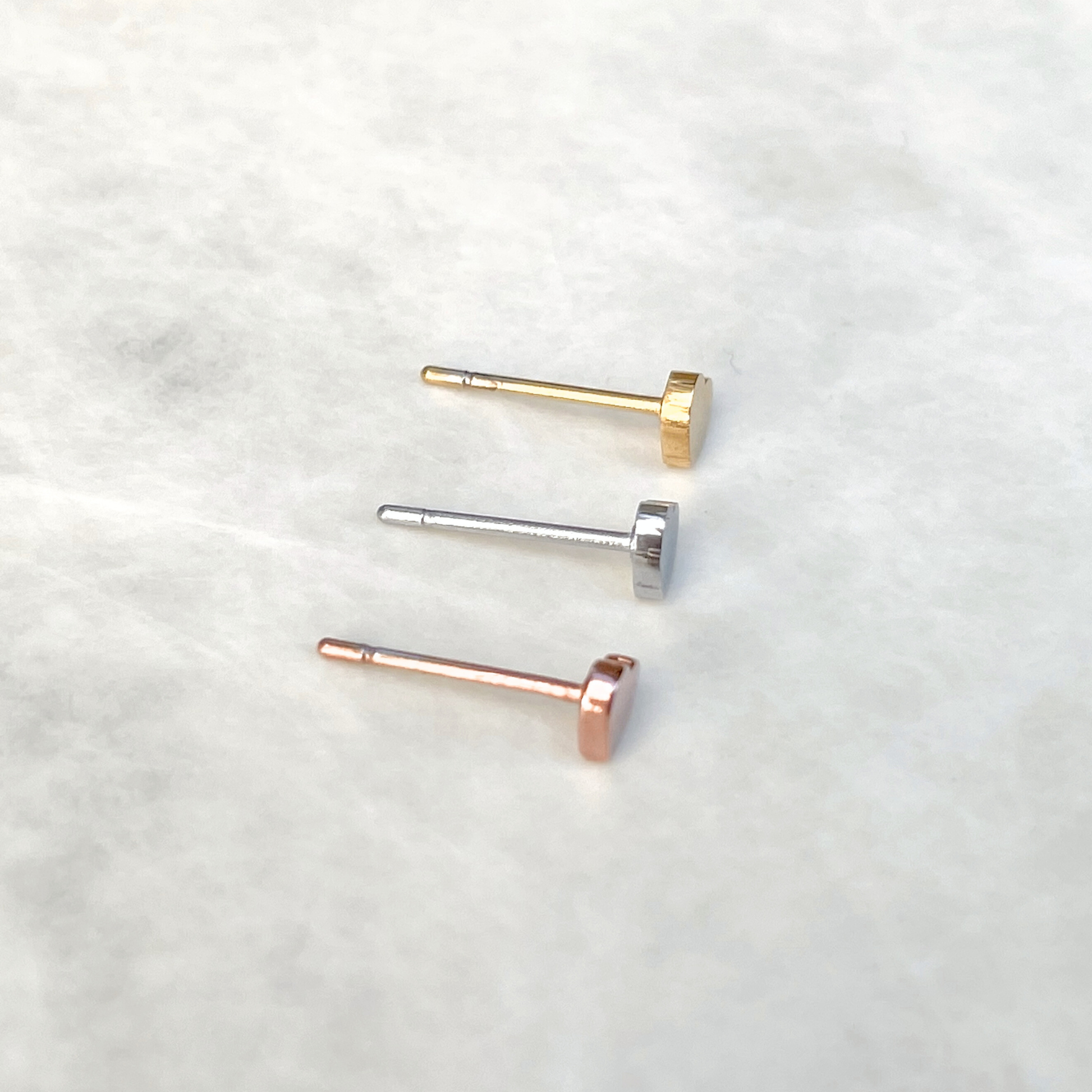 Top view of three heart earrings in gold, silver, and rose gold on a light background