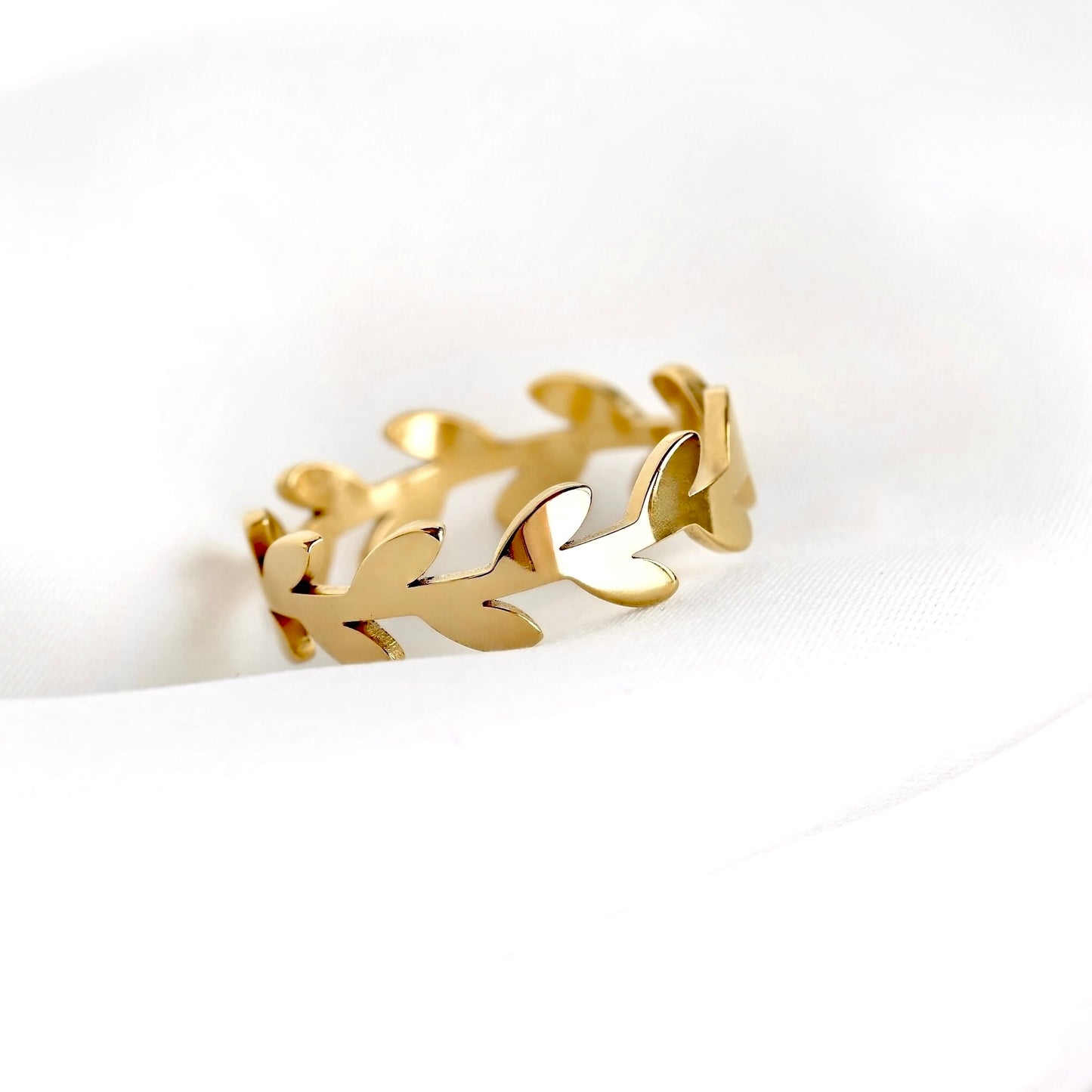 A gold leaf-patterned ring displayed on a soft, white textured fabric background.