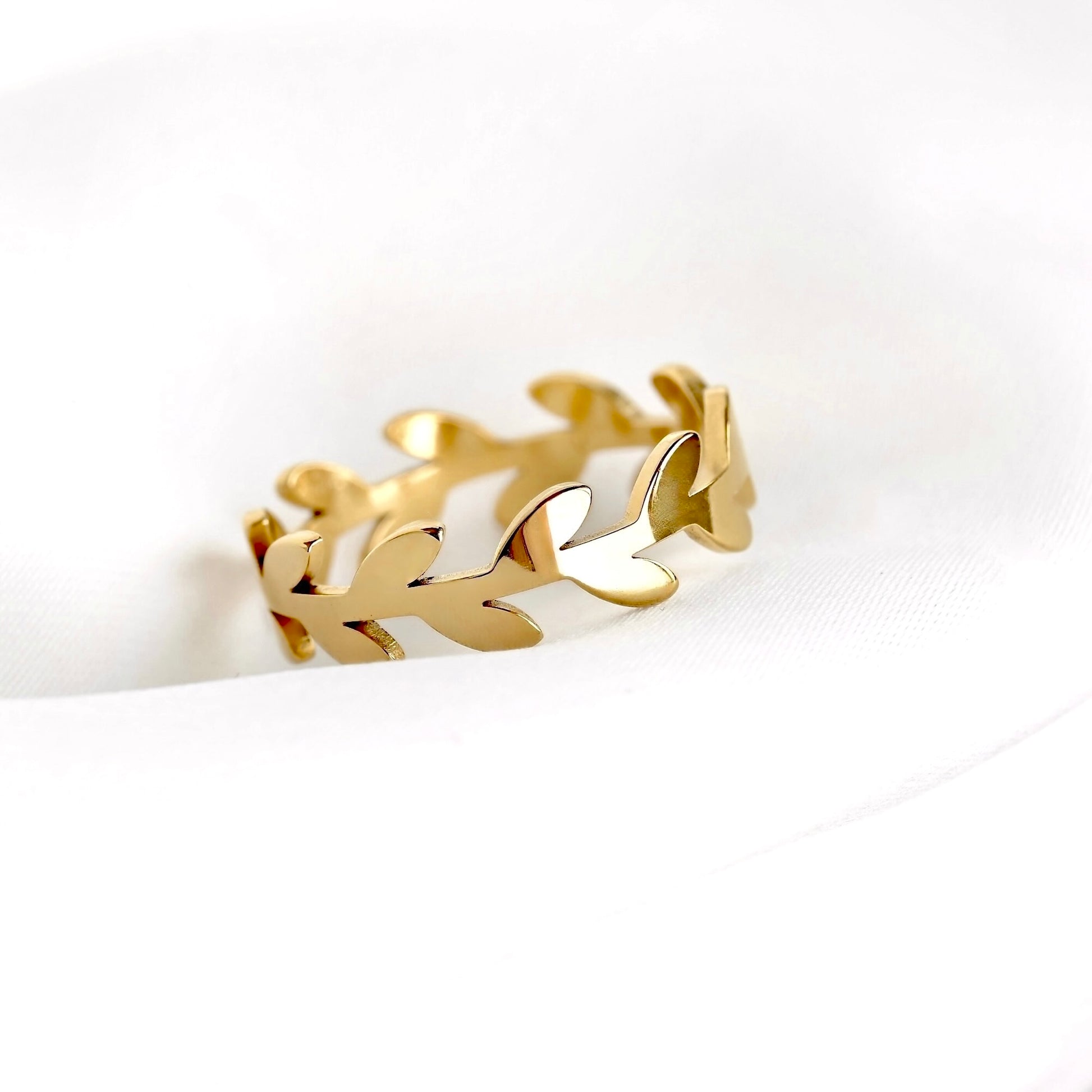 A gold leaf-patterned ring displayed on a soft, white textured fabric background.