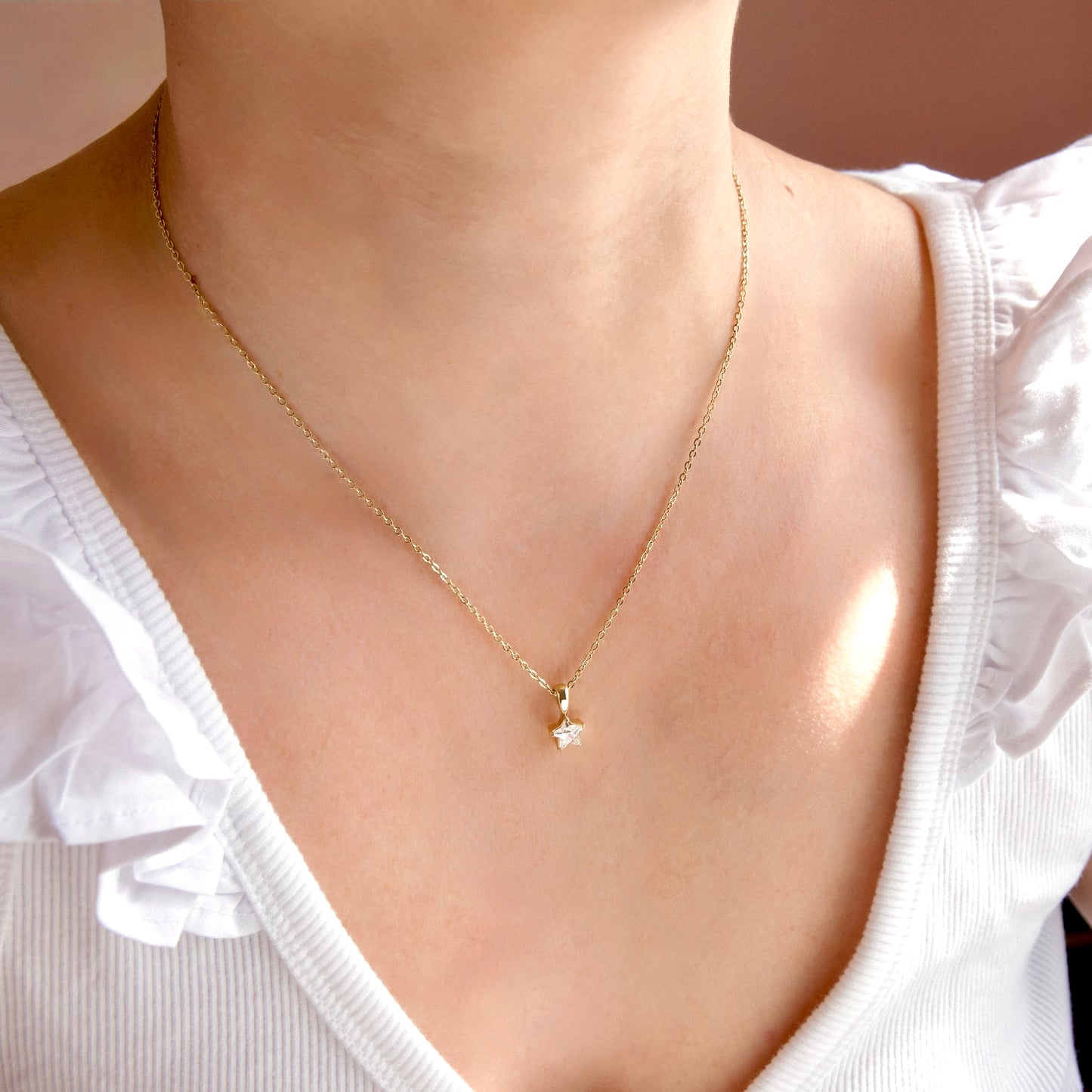 A close-up of a person wearing a delicate gold chain necklace with a small star-shaped pendant, styled with a white ruffled top.