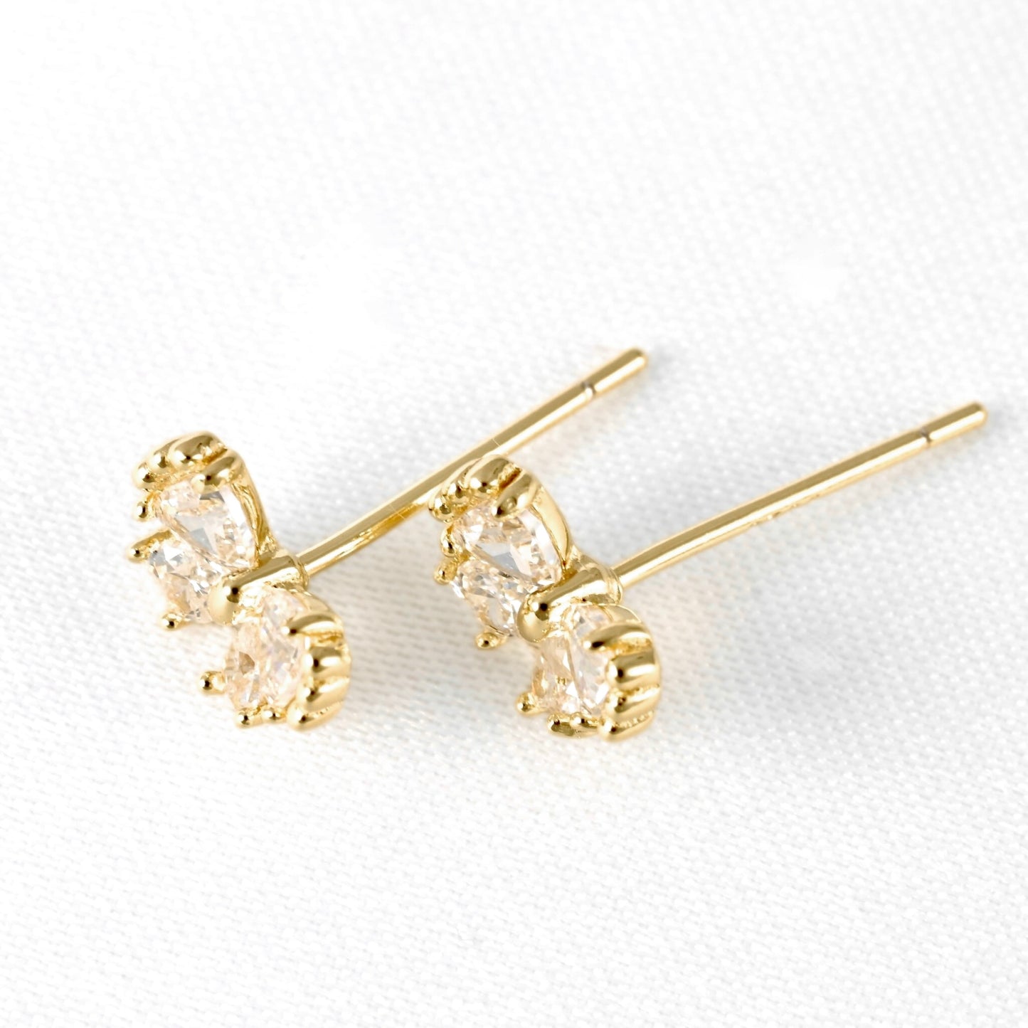 A pair of gold stud earrings with marquise-cut clear gemstones in a prong setting, displayed on a textured white background.
