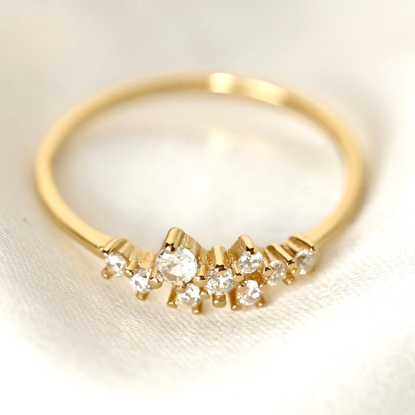 A gold ring with a curved row of clear gemstones, photographed close-up on a soft white fabric background.