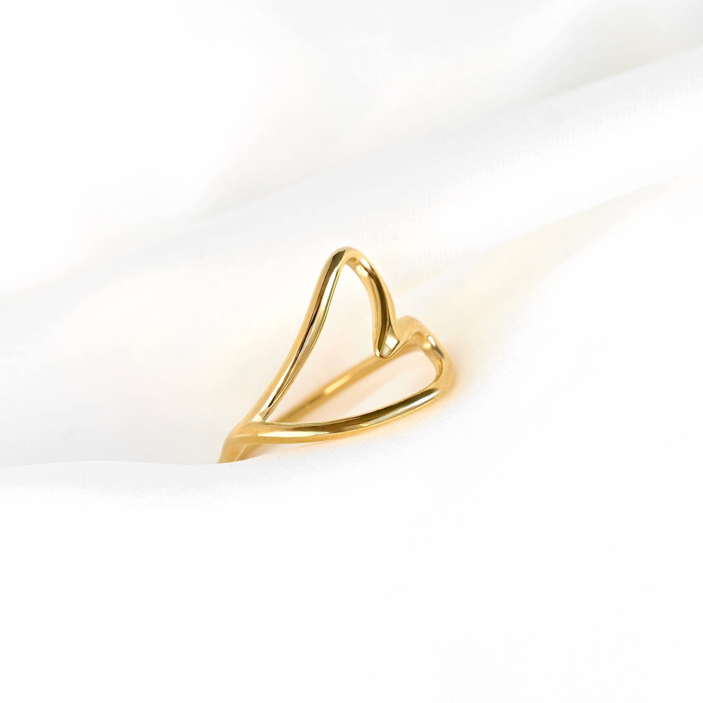 Close-up view of a gold-tone heart ring with the heart lying sideways on a white satin fabric