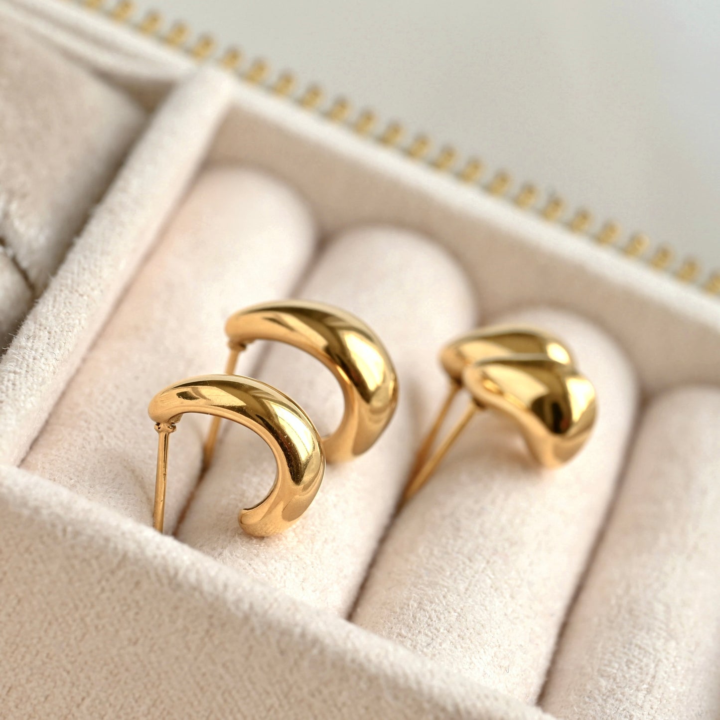 Side view of small and medium size gold dome earrings on a soft, beige jewelry box