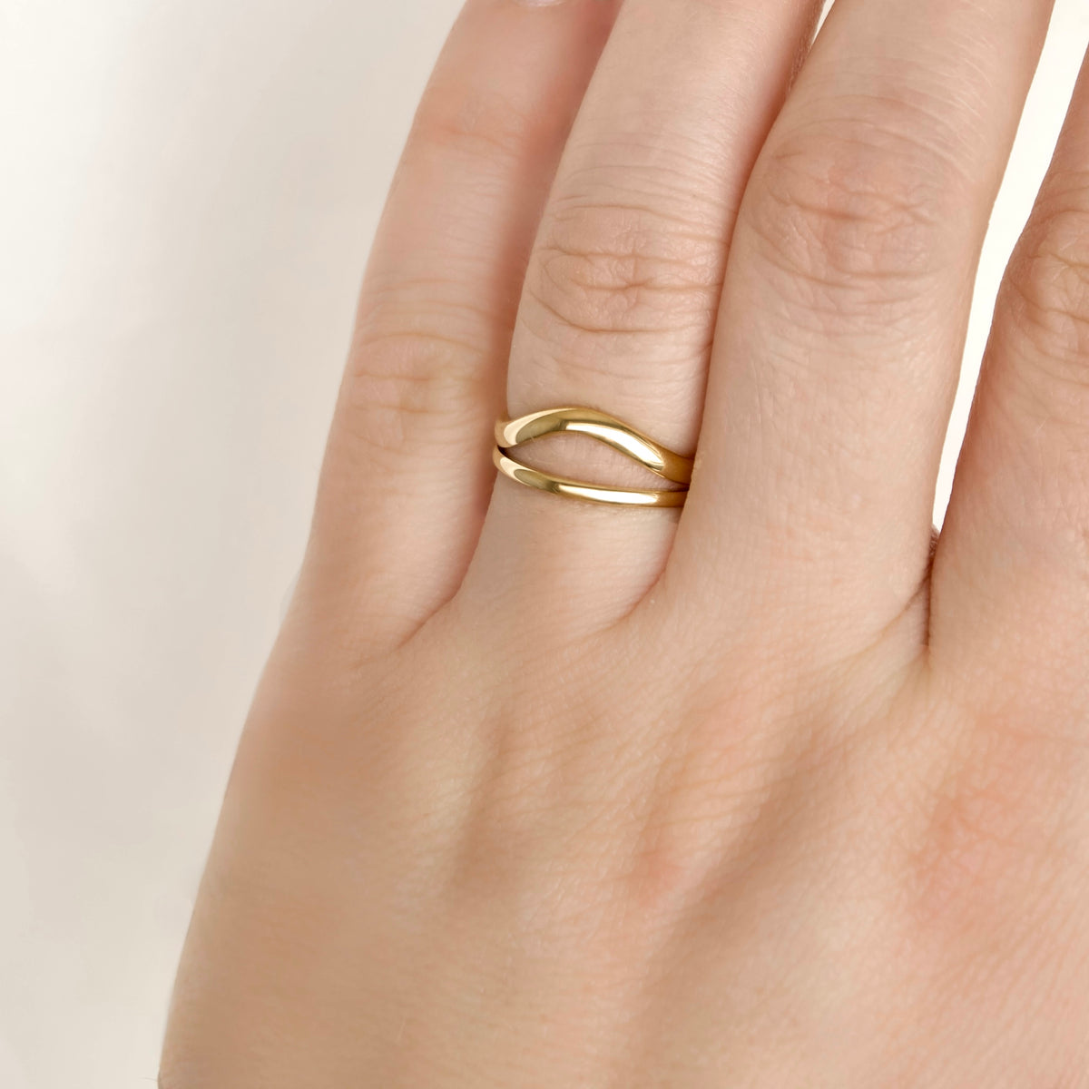 A close-up of a hand wearing a thin, double-band gold ring with a polished, wavy design.