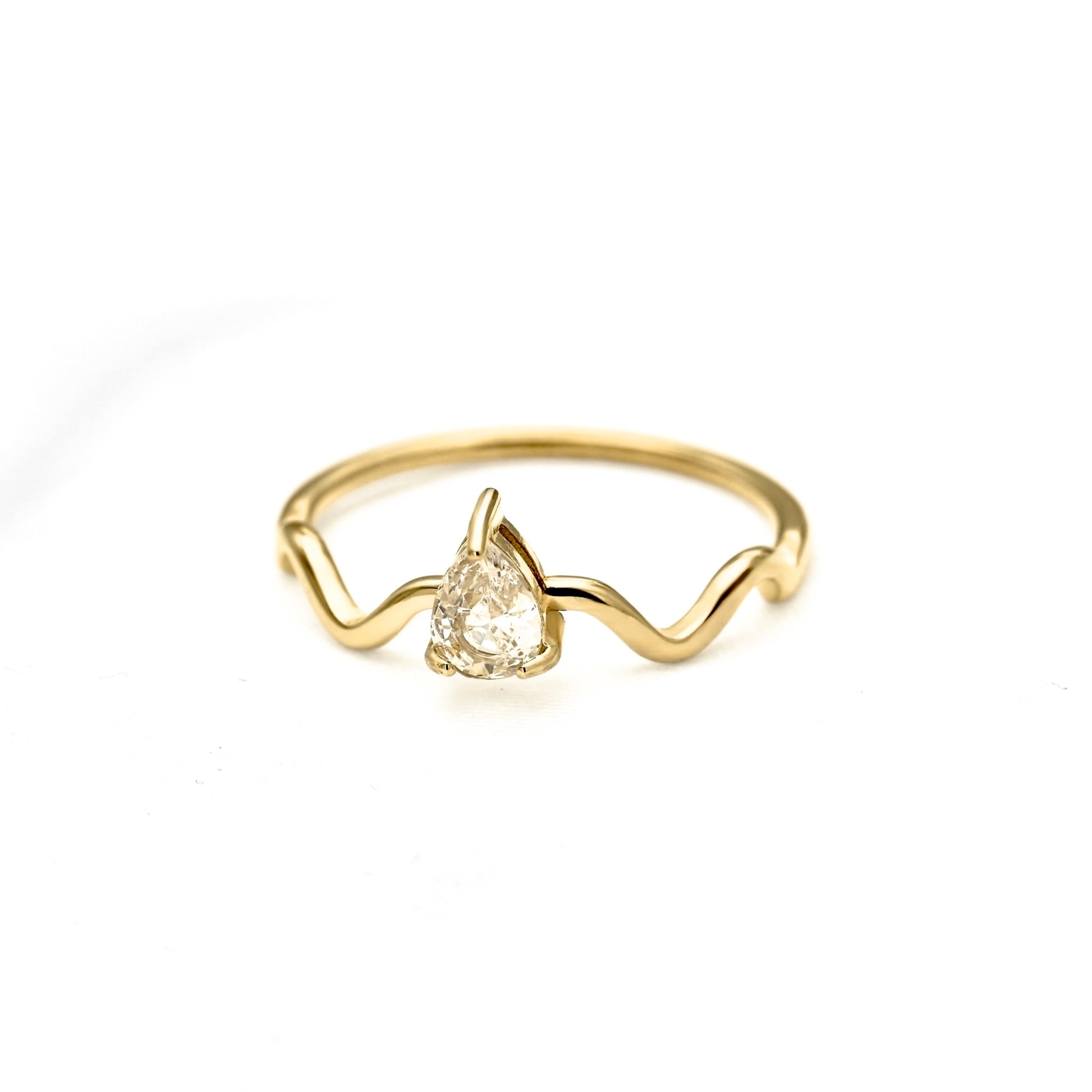 A gold wavy band ring featuring a central pear-cut clear gemstone, photographed on a clean white background.
