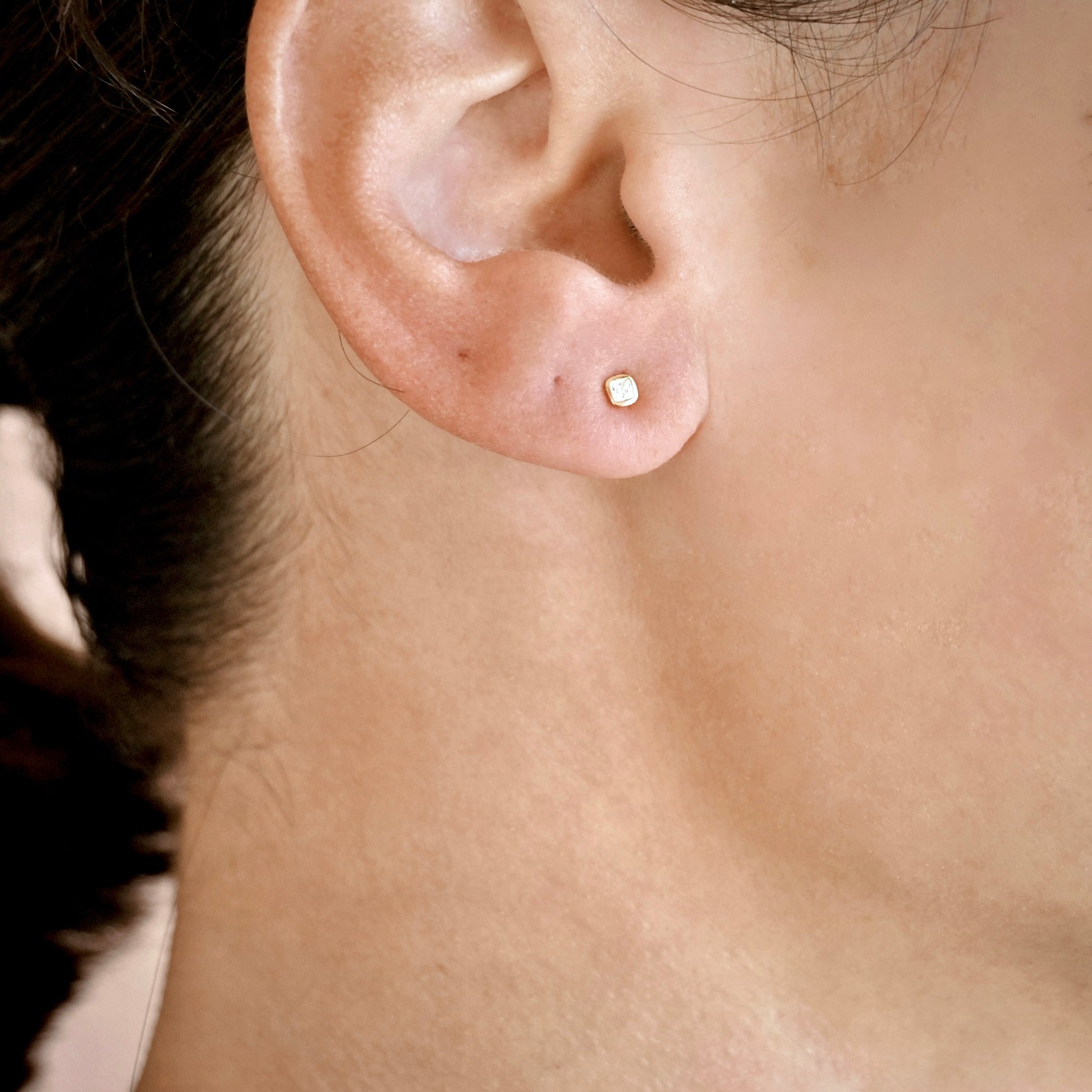 A close-up of a person's ear wearing a tiny gold stud earring with a small clear diamond.