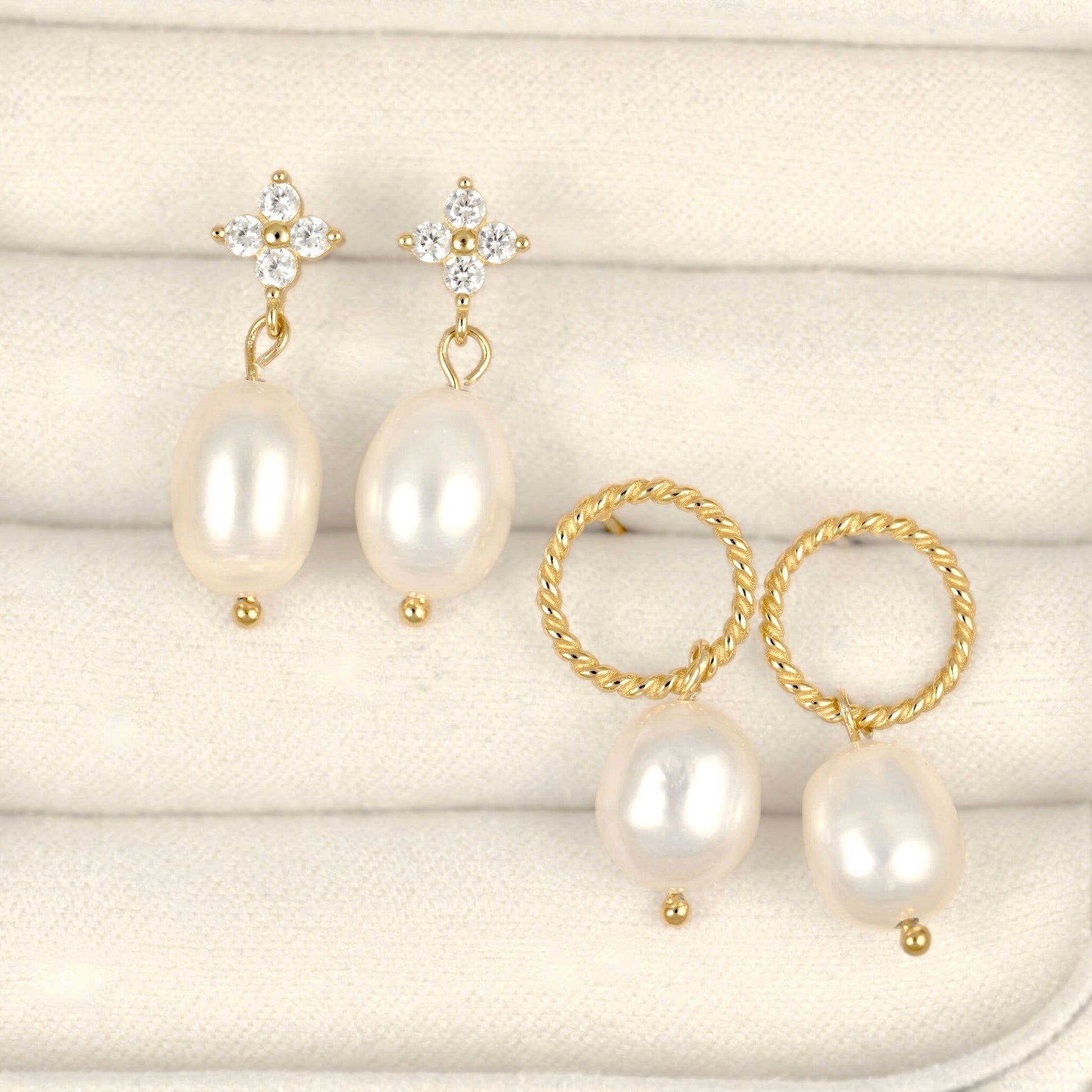 A pair of gold and pearl drop earrings with clear rhinestone floral studs, shown alongside a matching pair of gold hoop earrings with twisted rope edges and large irregular white pearls, arranged on a cream textured fabric background.