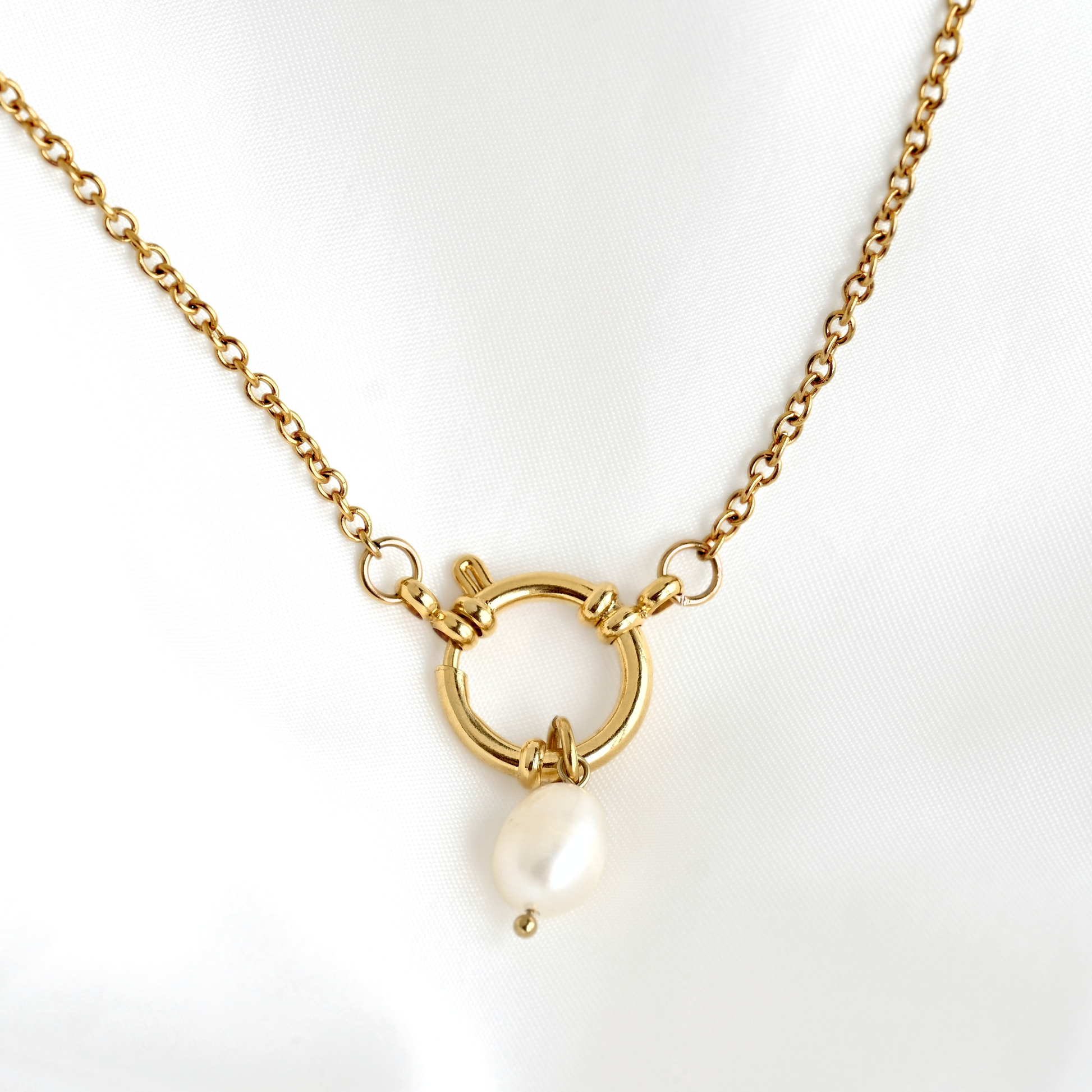 A gold sailor clasp chain necklace featuring a small white pearl hanging from it, displayed on a white fabric background.