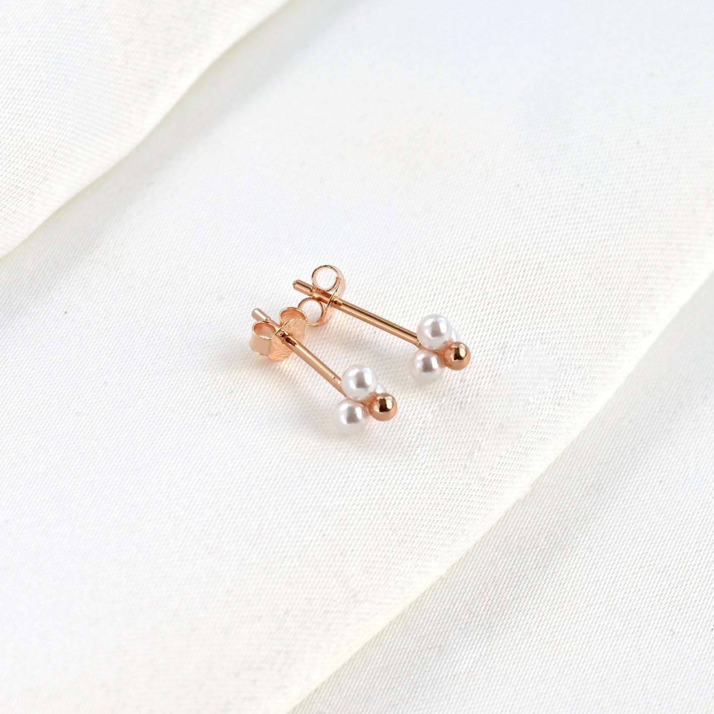 Tope view of rose gold pearl earrings on a white fabric background