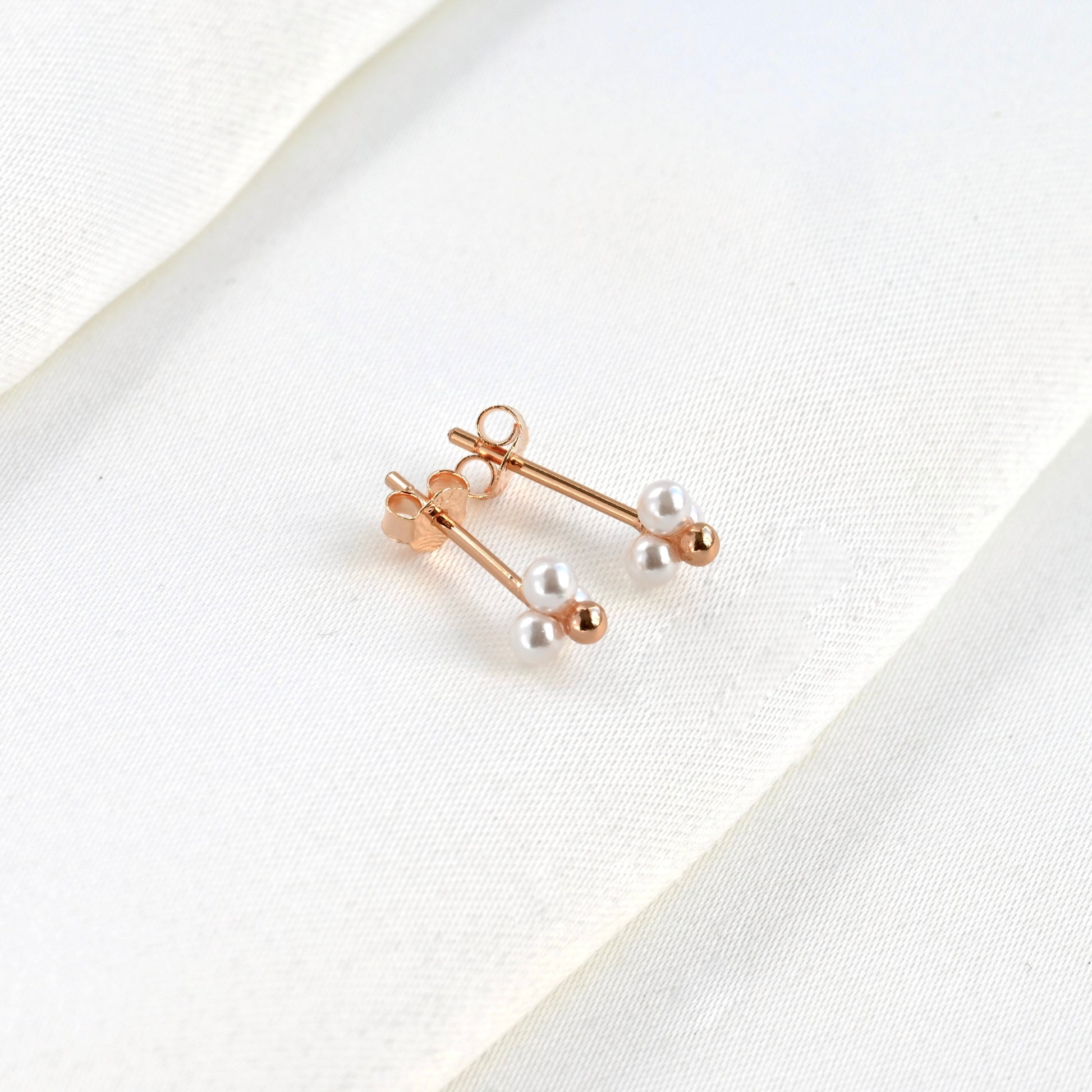 Tope view of rose gold pearl earrings on a white fabric background