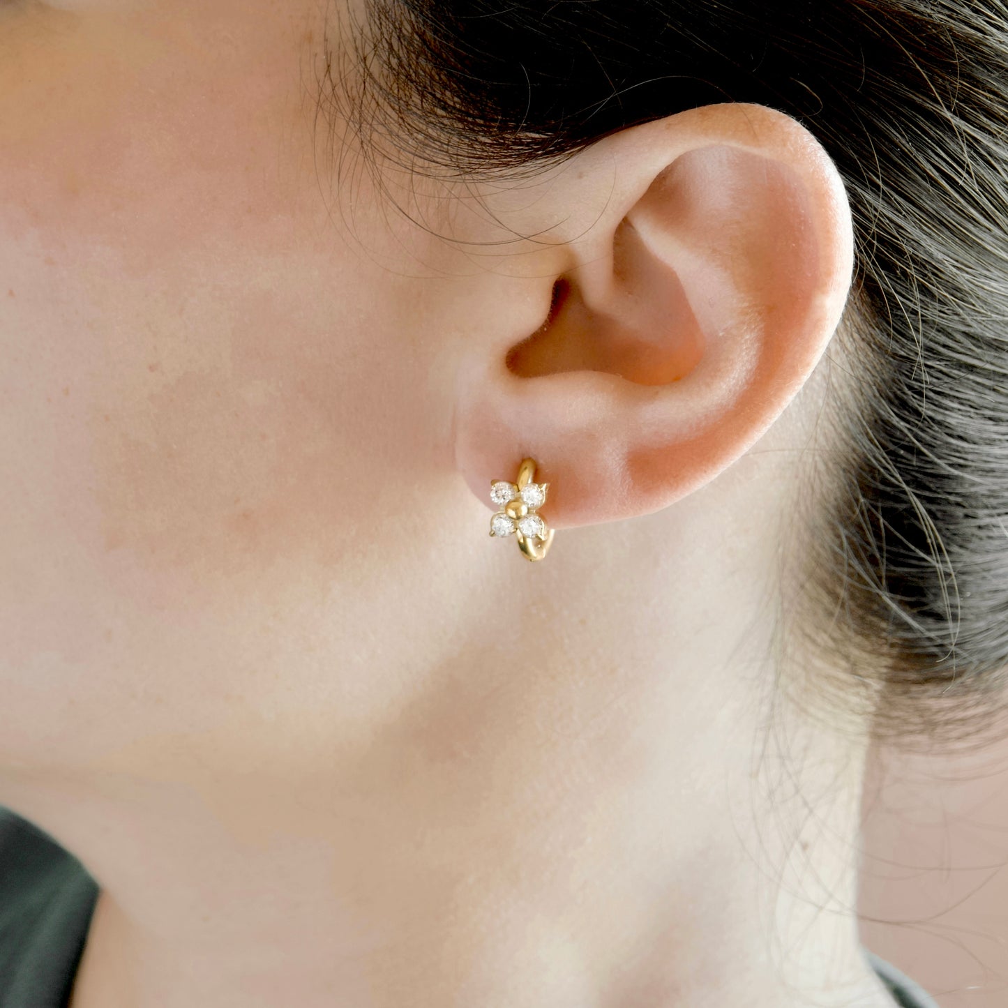 A close-up of a person's ear wearing a small gold flower-shaped stud earring with clear stones.