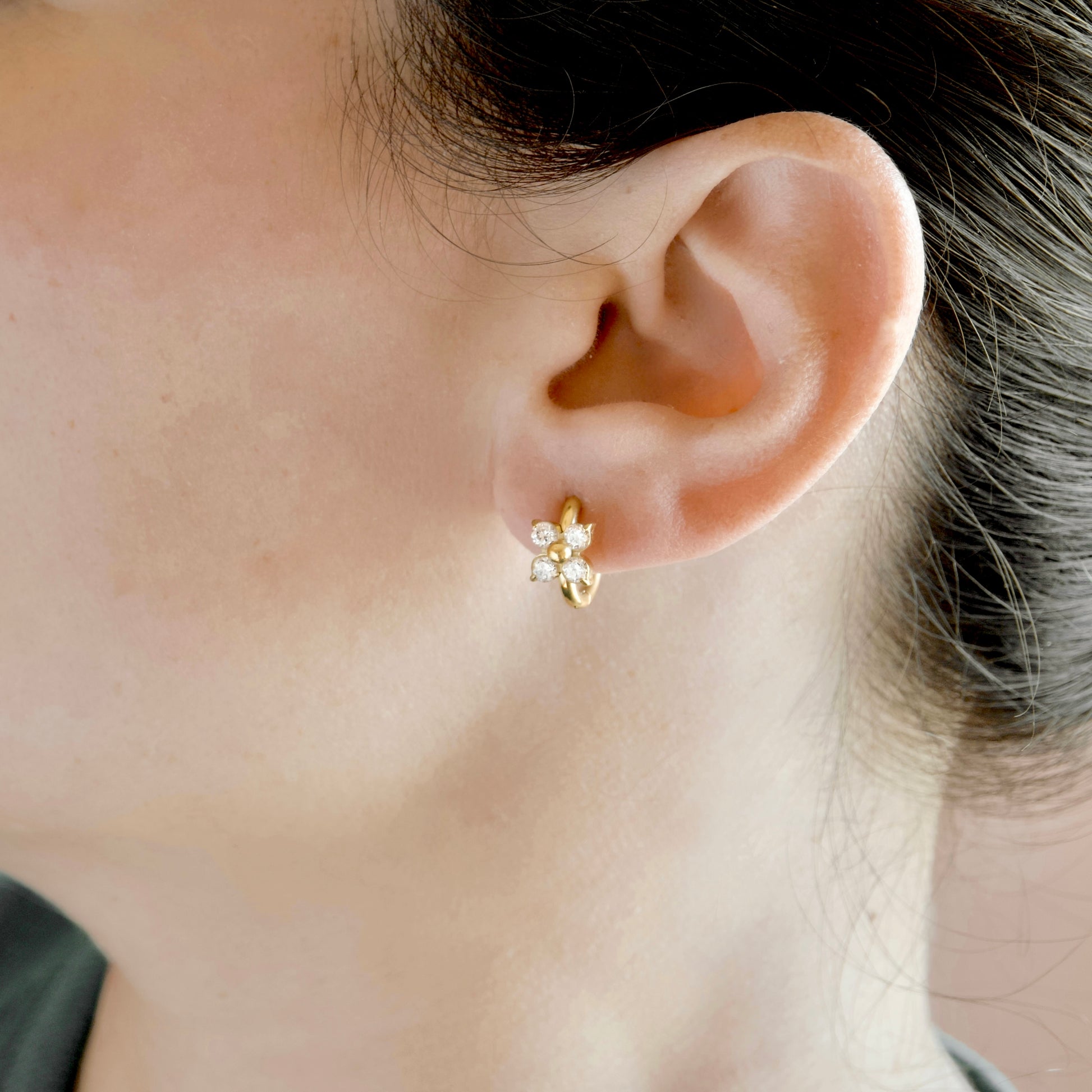 A close-up of a person's ear wearing a small gold flower-shaped stud earring with clear stones.