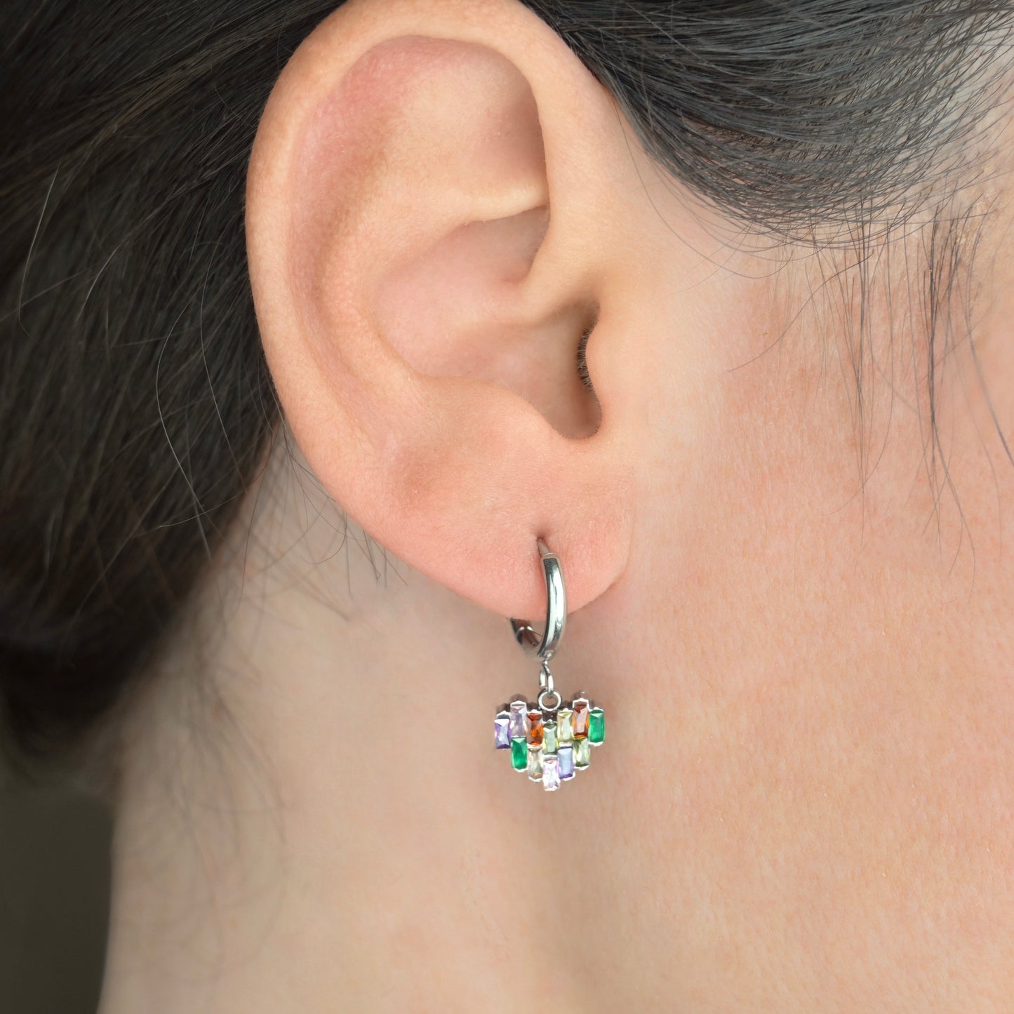 Close-up of an ear wearing a heart-shaped earring with colorful stones.