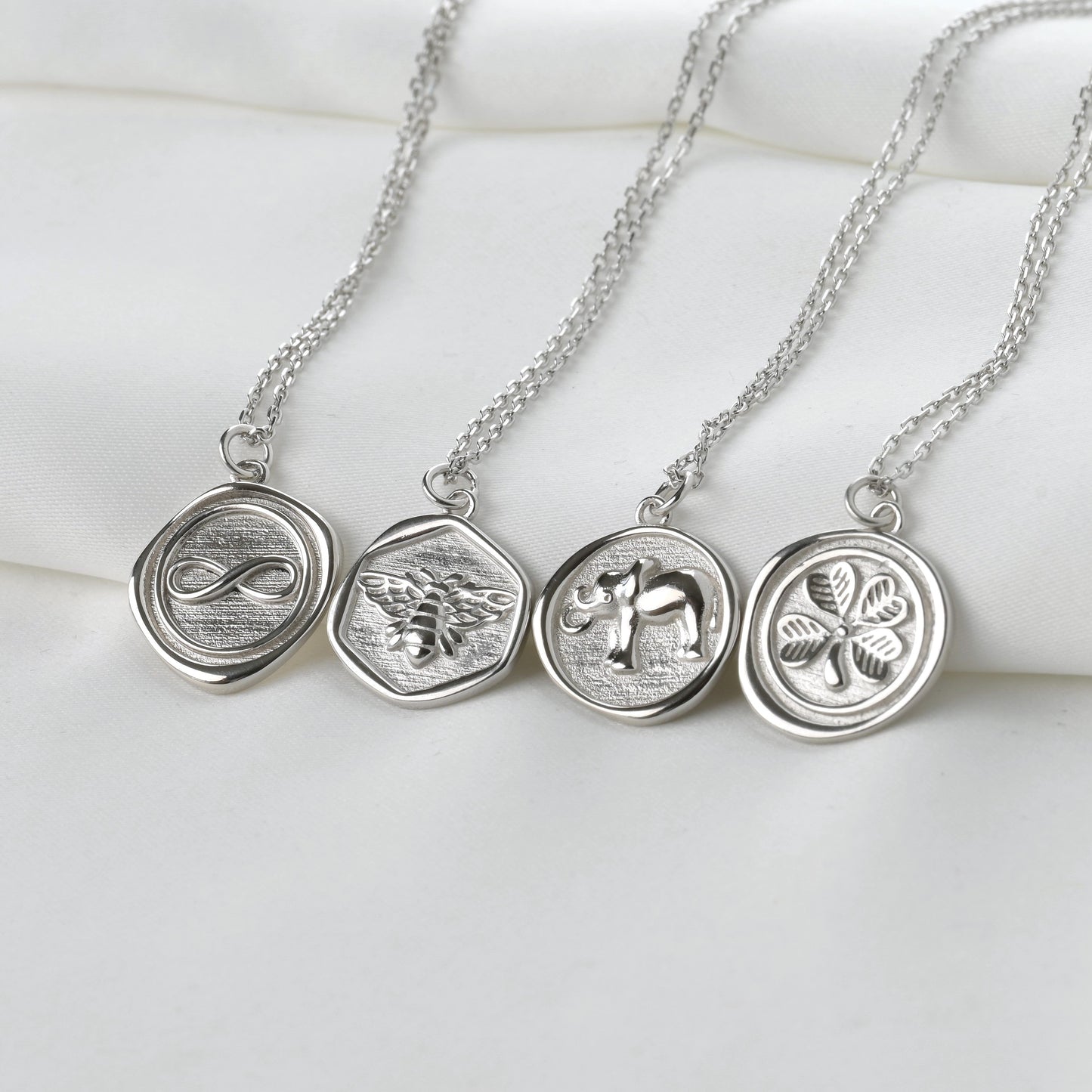 Three silver necklaces with circular pendants on a white surface