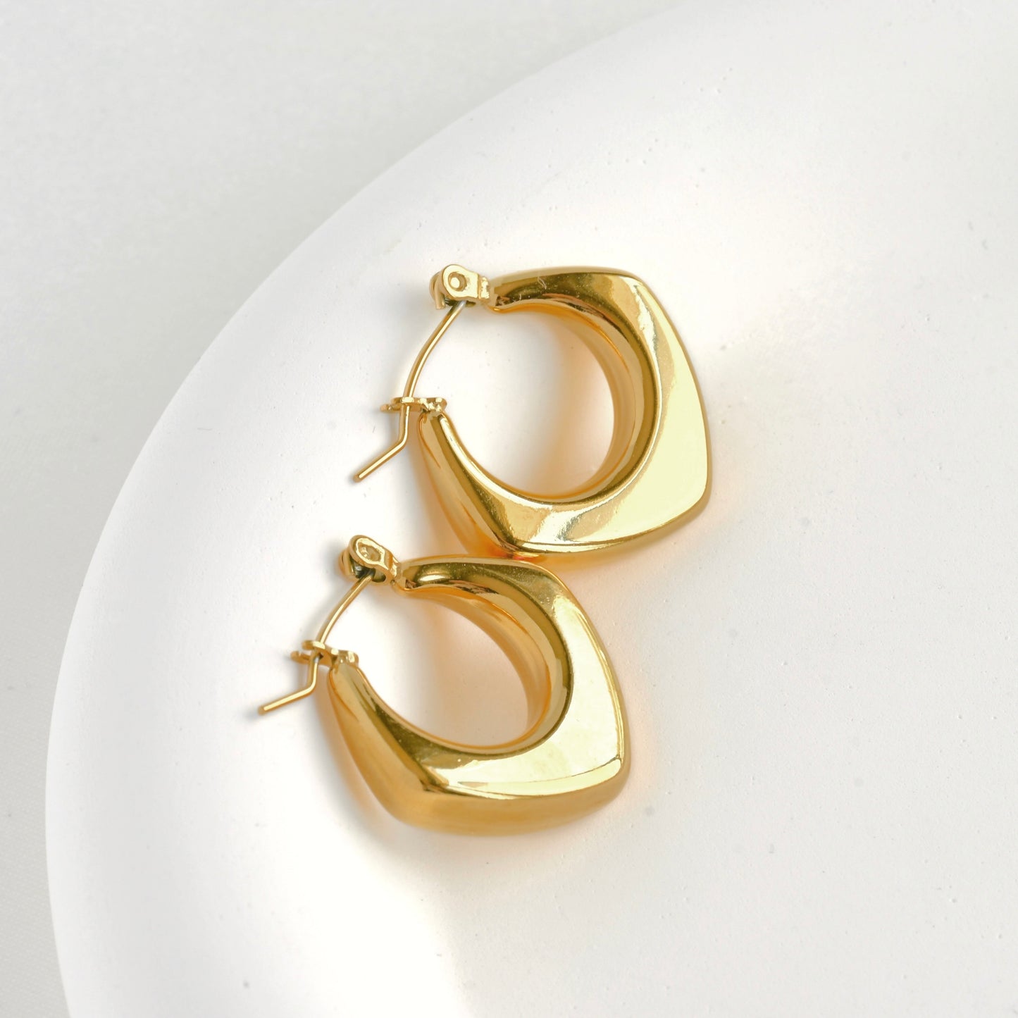 Top view of gold square hoop earrings on a white plate