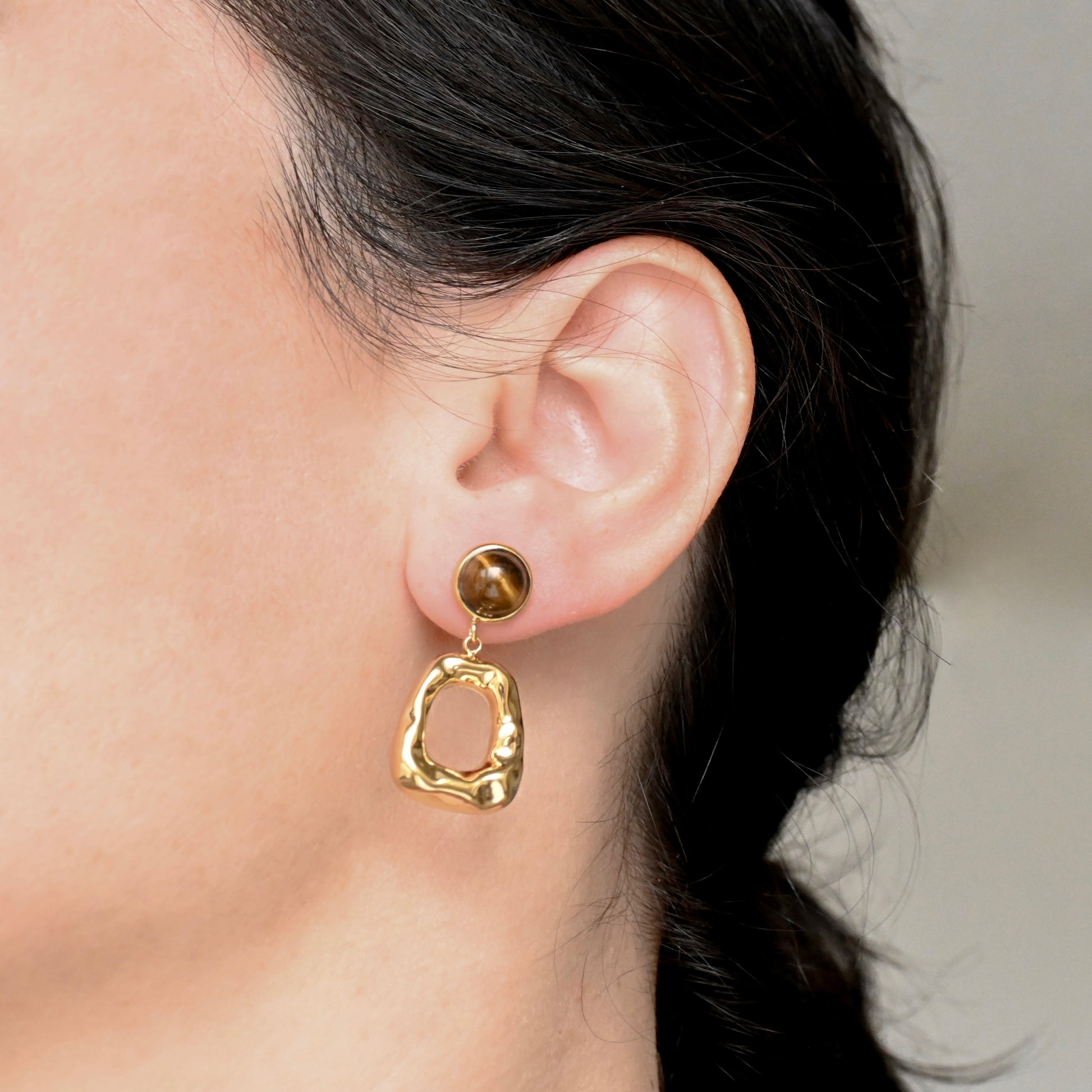 Gold figure earring with brown gemstone worn by a person with a neutral background