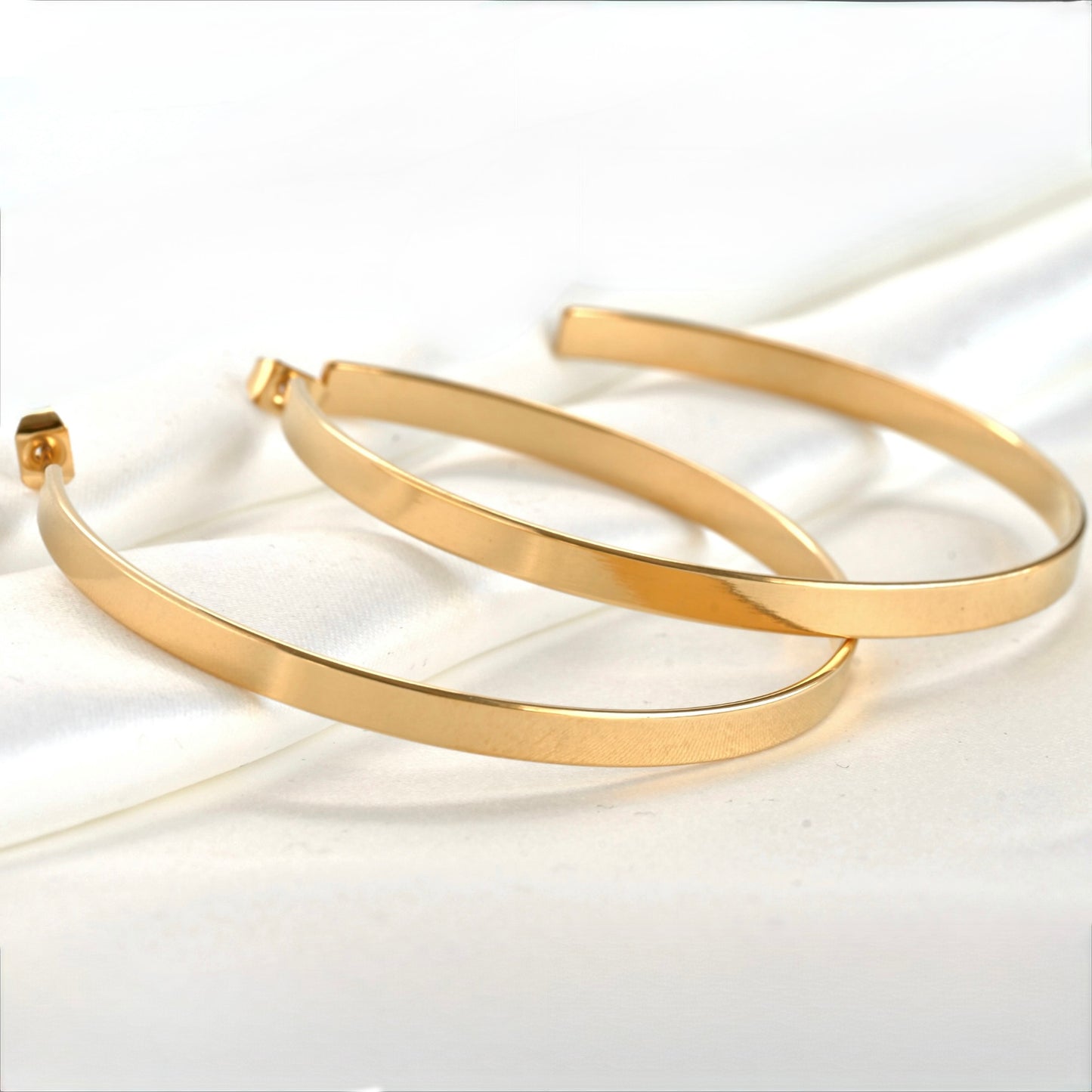 Two wide gold hoop earrings agaist folded white satin