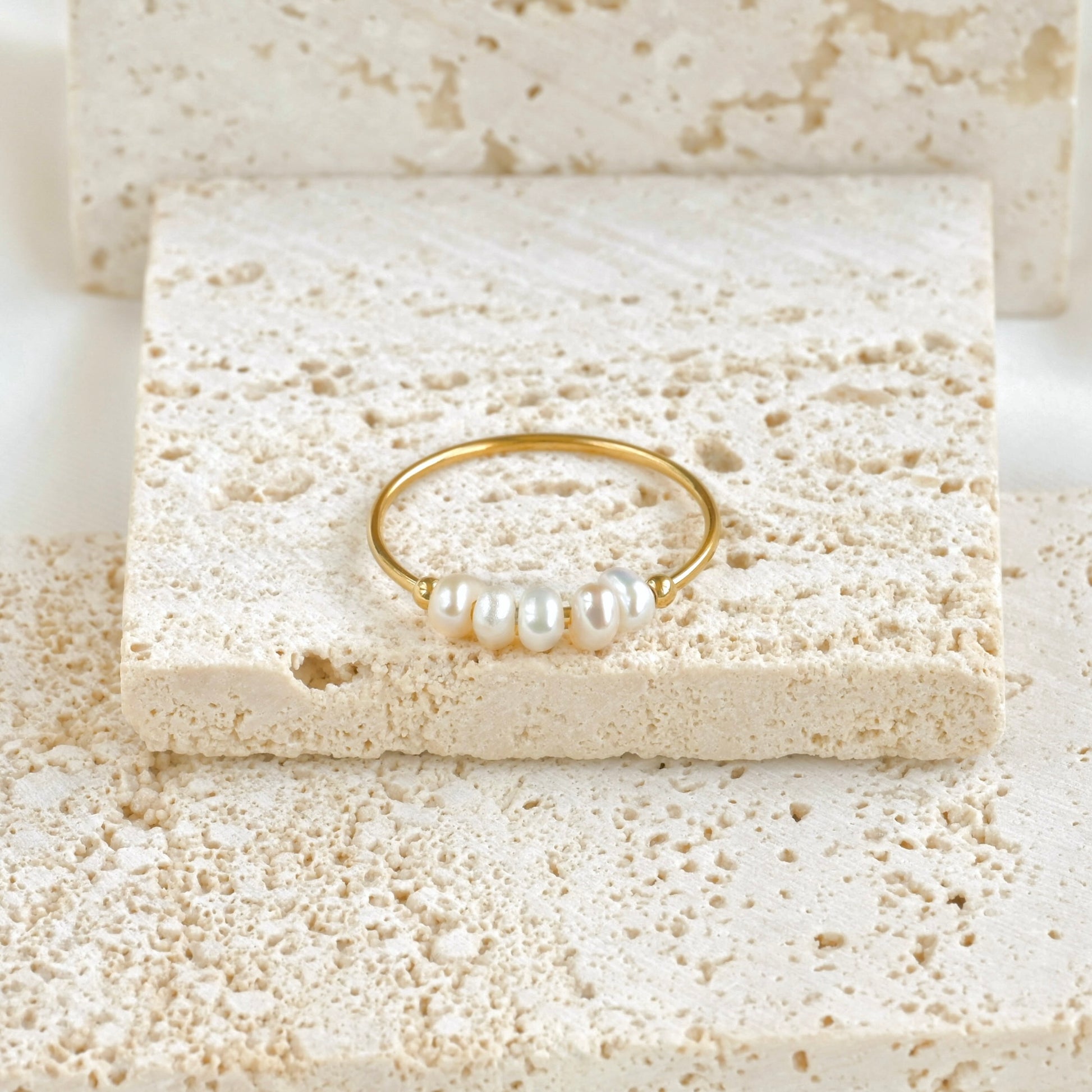 Dainty gold ring with 5 tiny natural pearls on a textured stone surface