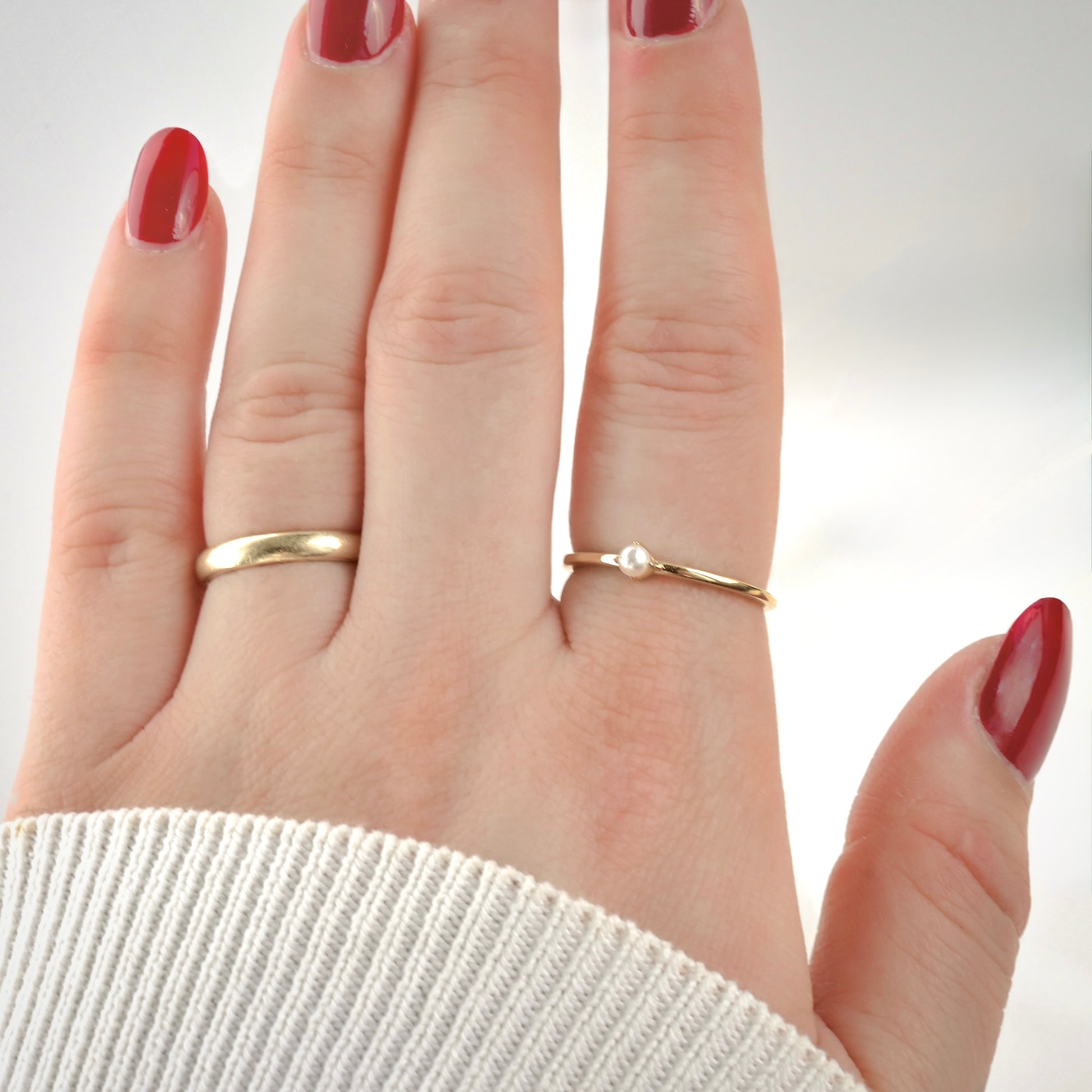 Hand wearing two gold rings , one with pearl one plain gold, with a light background