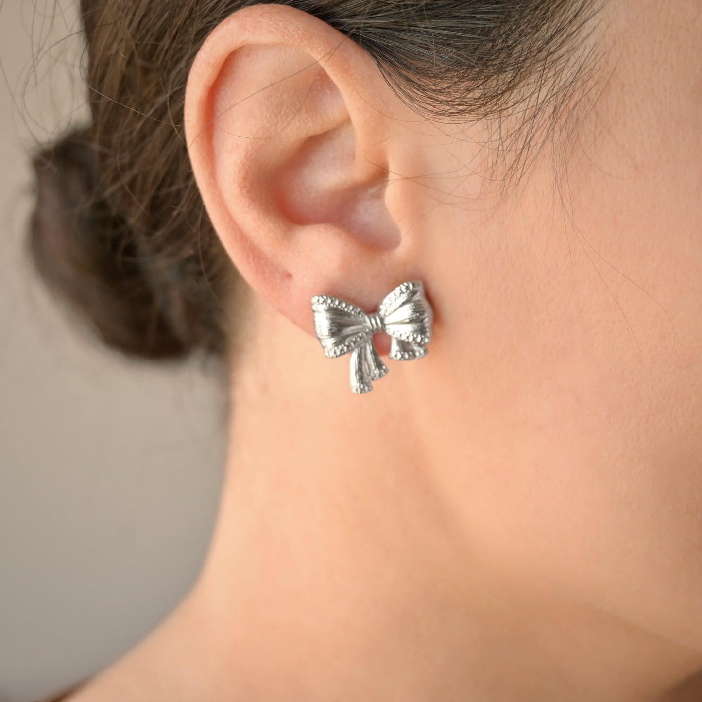 Silver bow-drop earrings worn by a person with a neutral background
