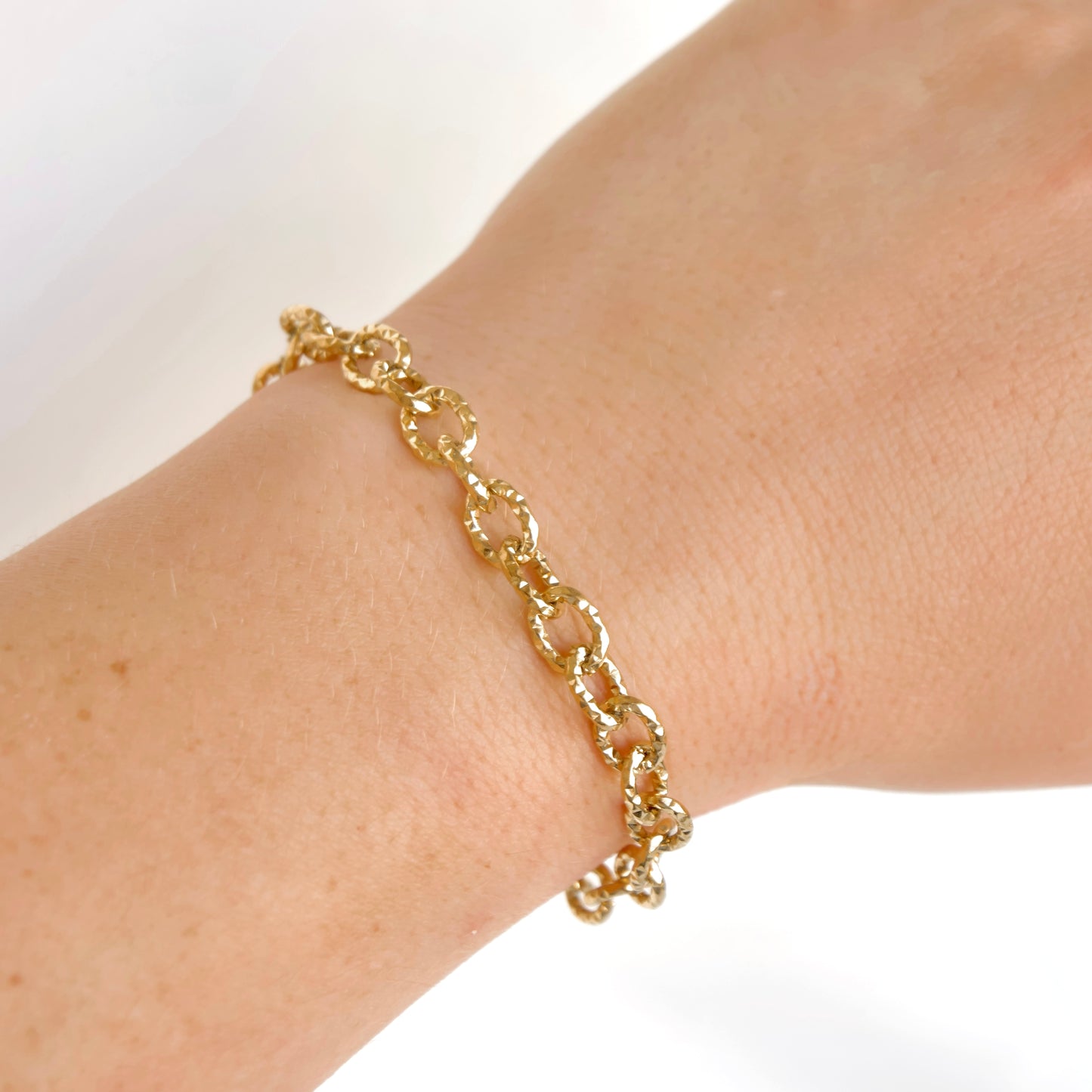 A close up view of a wrist wearing a fold chain bracelet with  large oval hammered links.