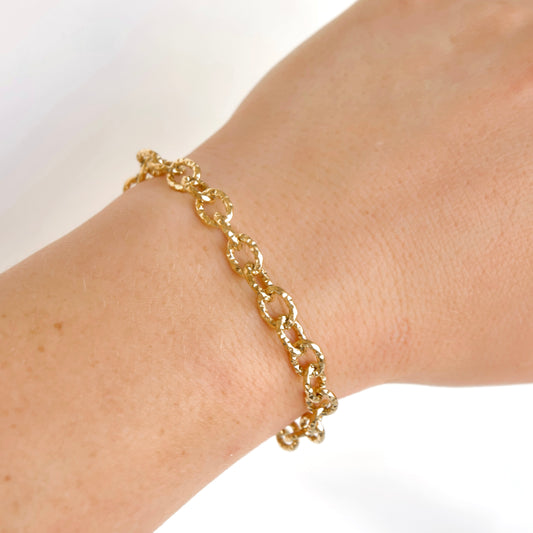 A close up view of a wrist wearing a fold chain bracelet with  large oval hammered links.