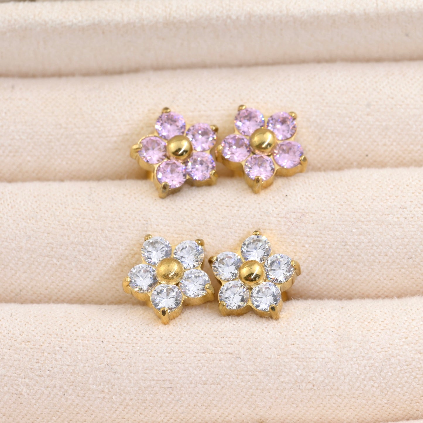 Close-up top view of two pairs of flower earrings with pink and clear CZ stones on a beige surface
