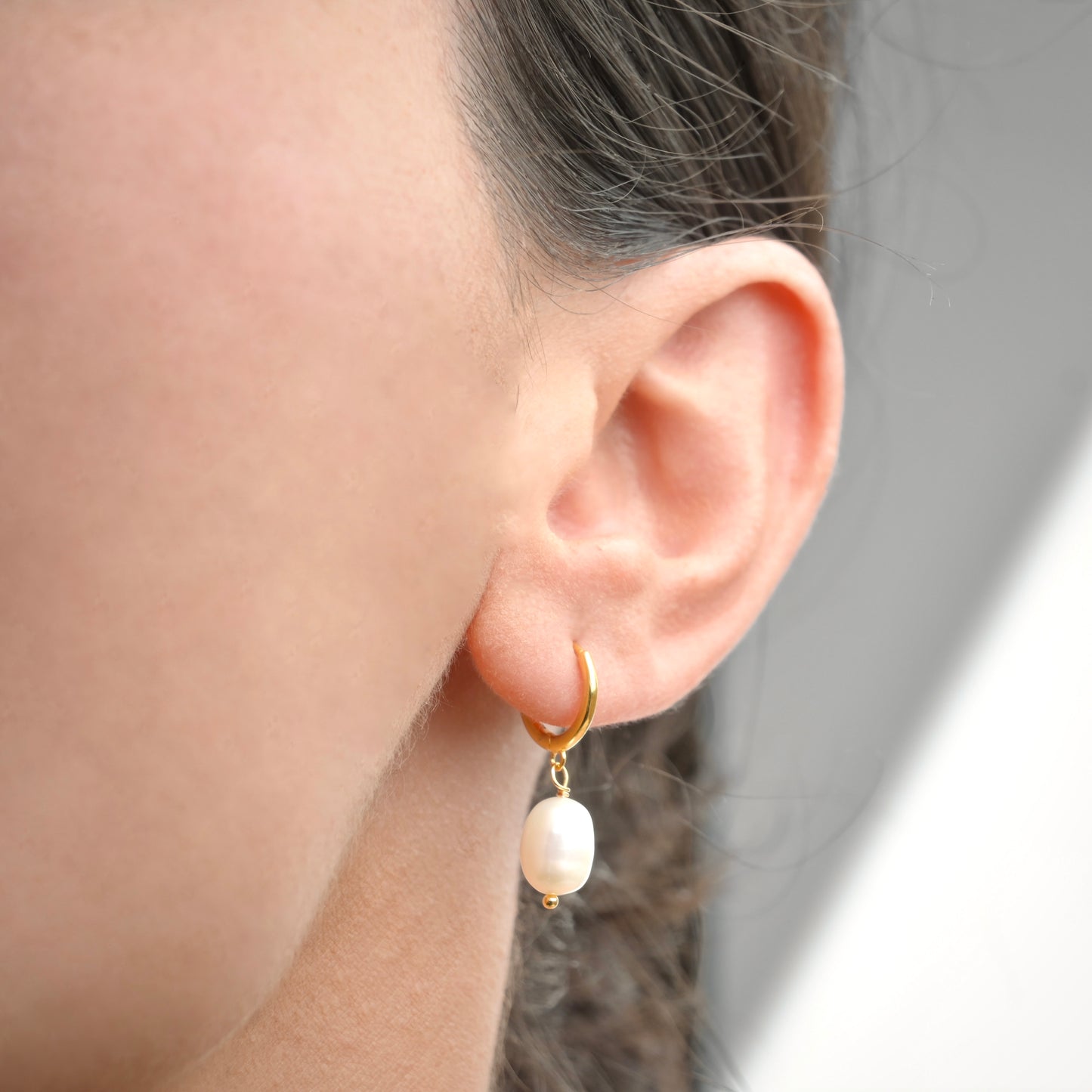 Close-up of an ear wearing a gold earring with a pearl drop.