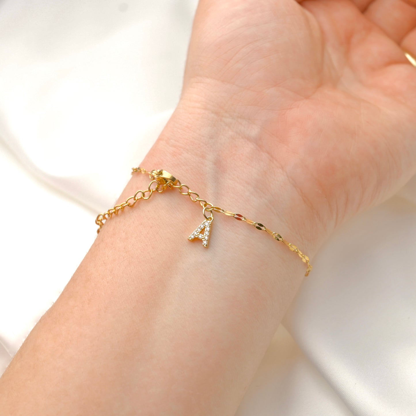 Gold mirror chain bracelet with a diamond  letter 'A' charm on a wrist against a white background