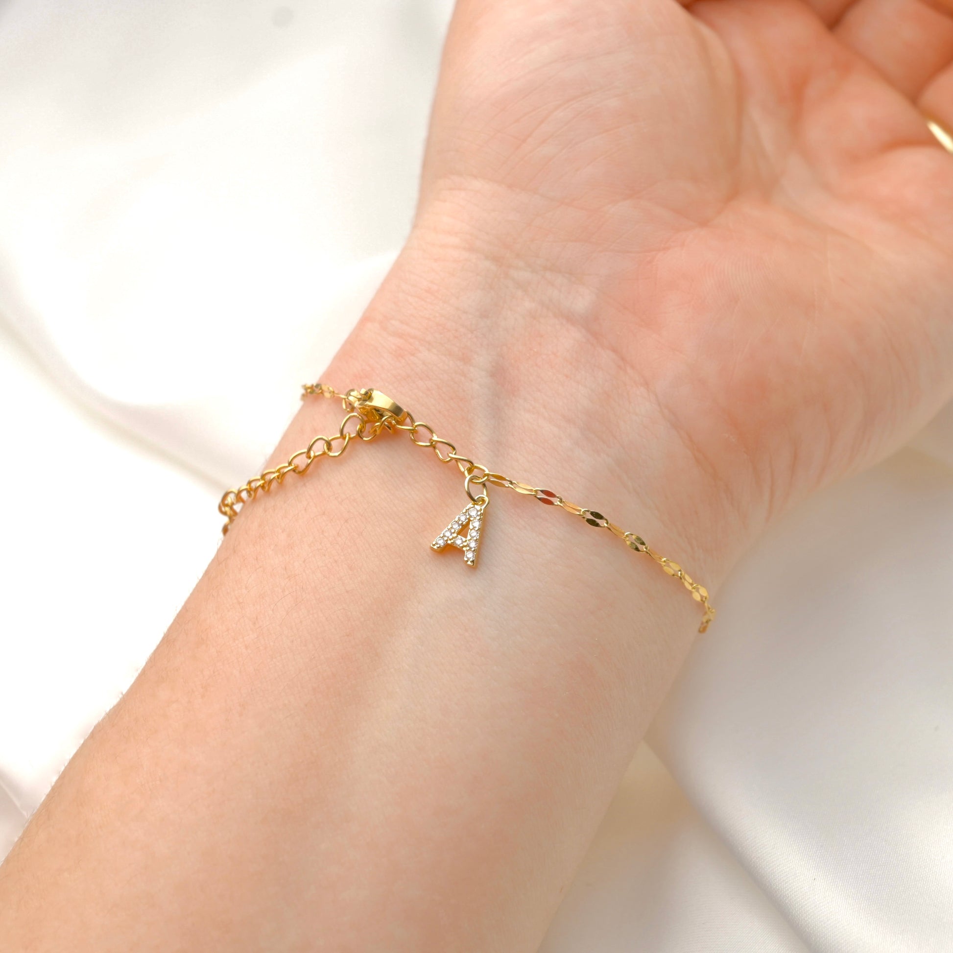 Gold mirror chain bracelet with a diamond  letter 'A' charm on a wrist against a white background
