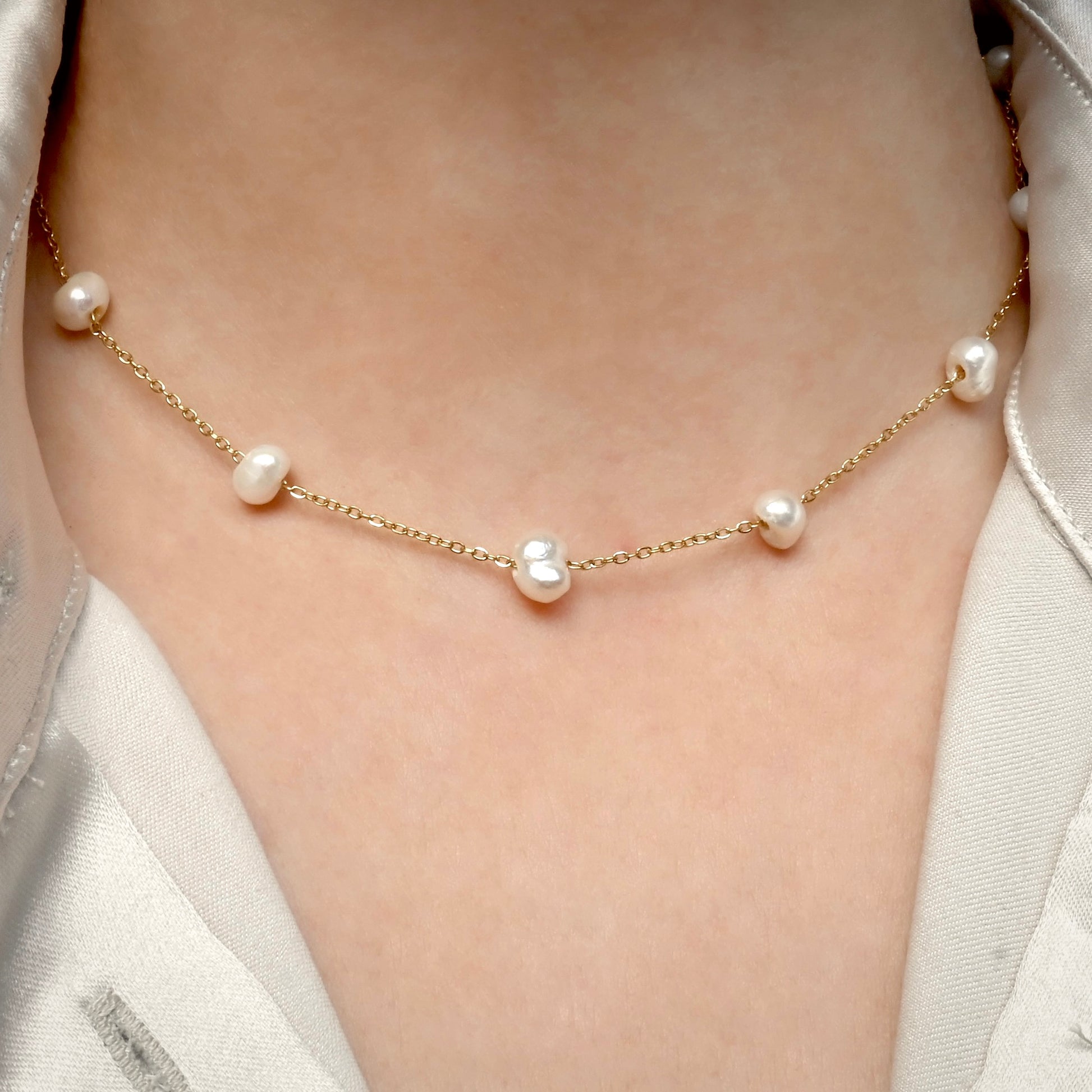 Pearl necklace with gold chain on a person wearing a light-colored satin shirt