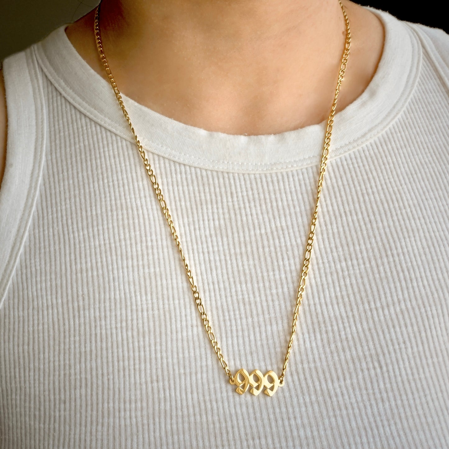 Gold figaro necklace with '999' charm worn by a person on a white background