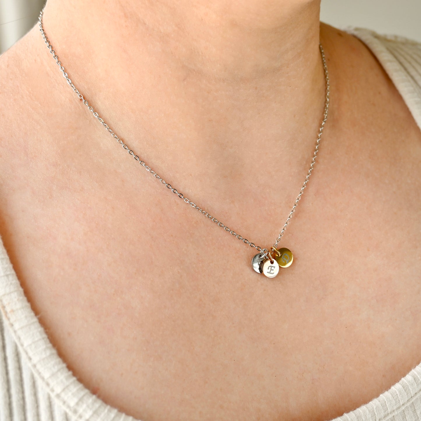 Personalized  two tone necklace with circular initial pendants on a person wearing a light-colored top.